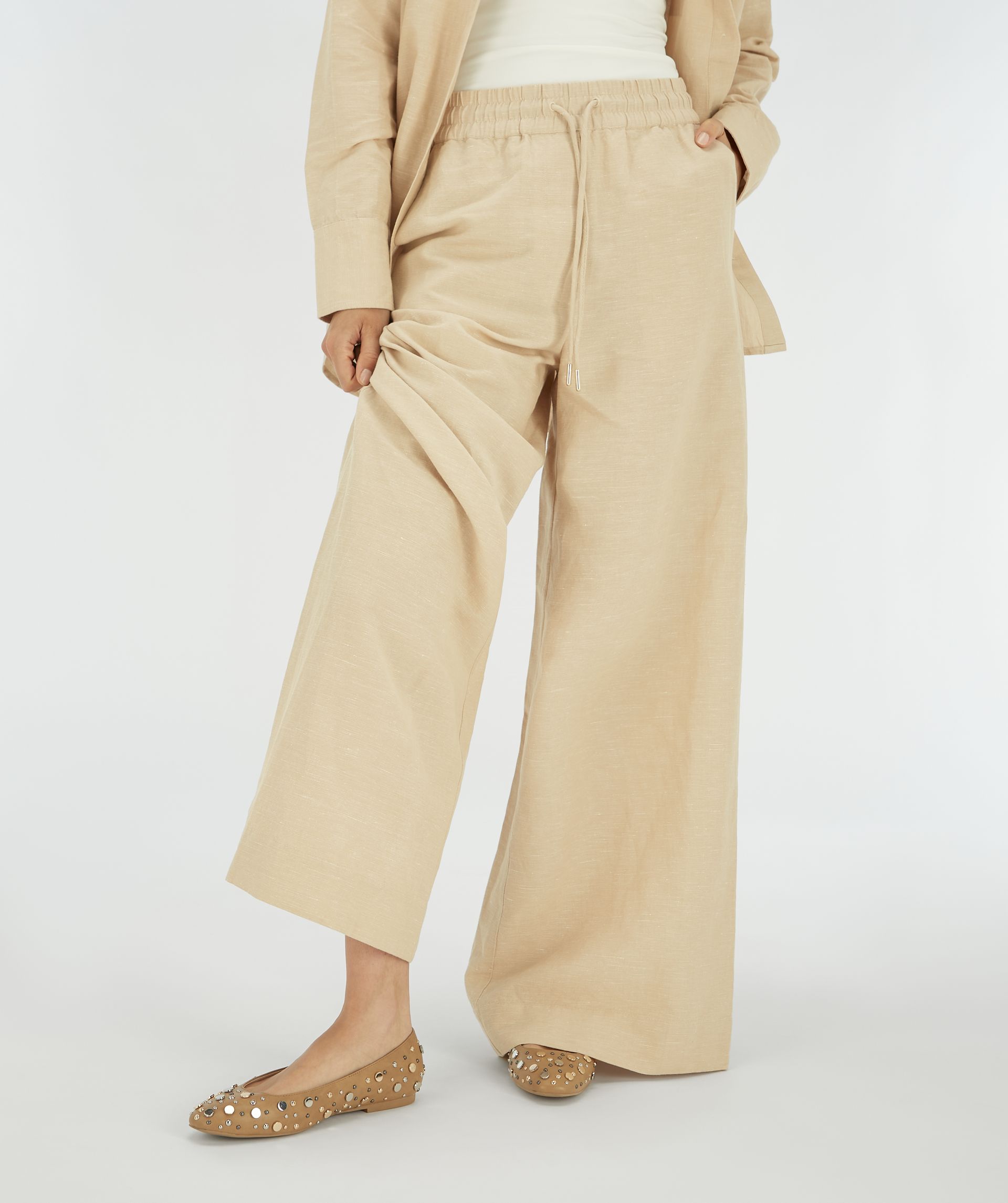 Model draagt beige ballerina's met studs gecombineerd met beige wide leg broek.