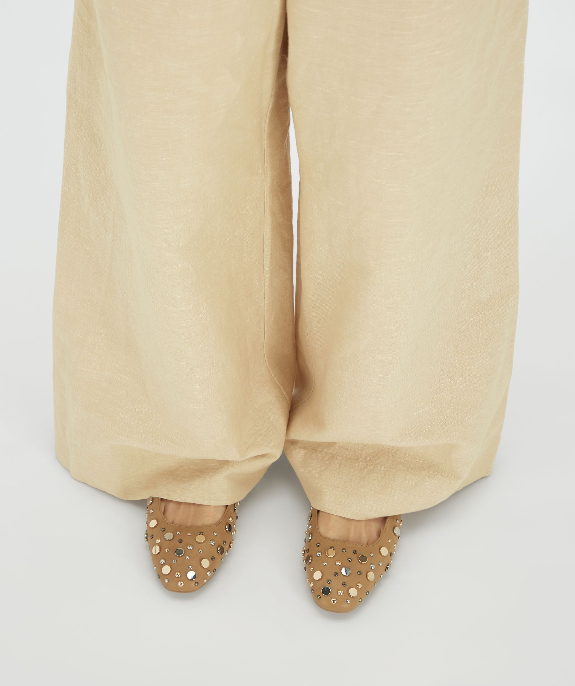 Model draagt beige ballerina's met studs gecombineerd met beige wide leg broek.