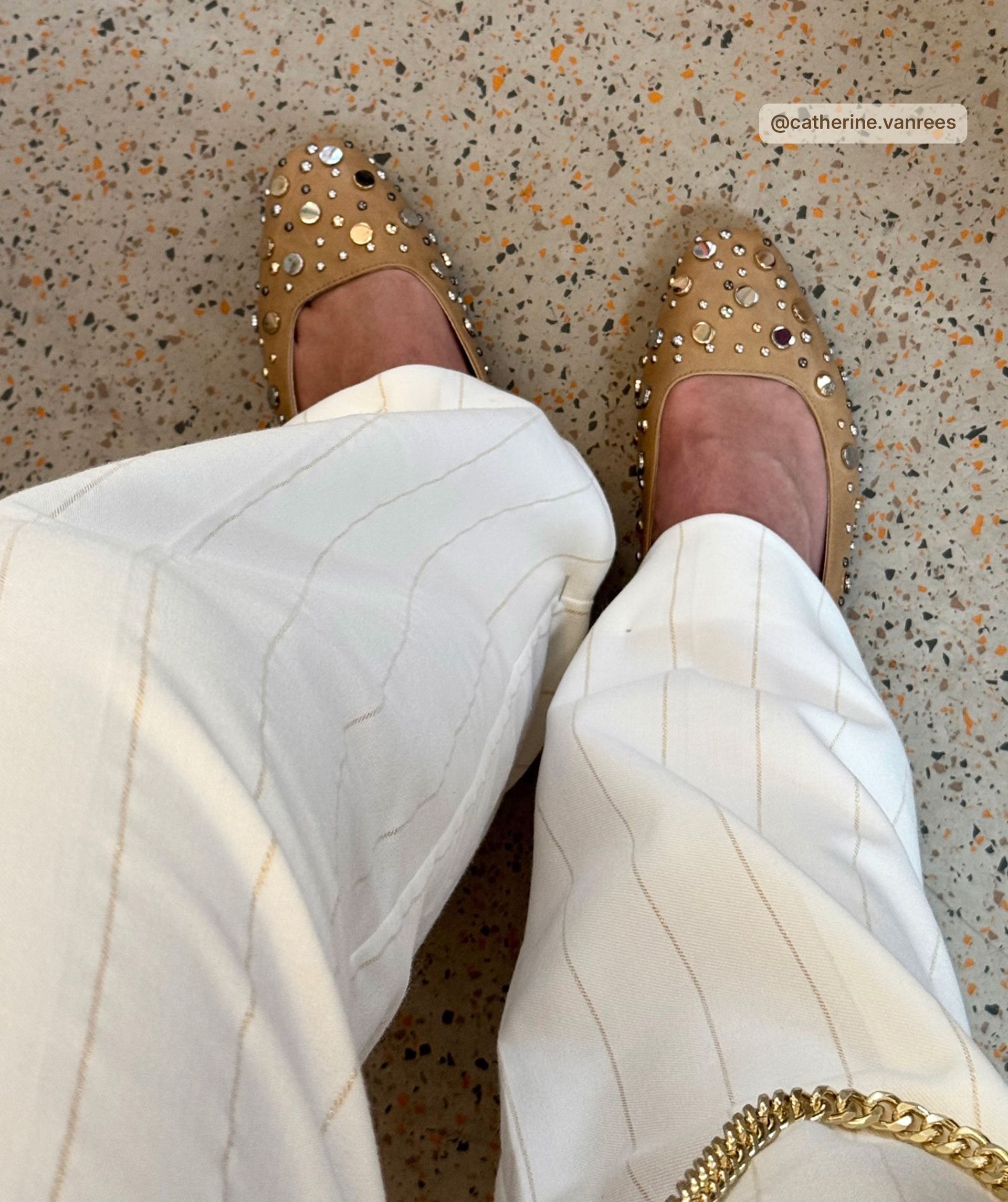 Influencer draagt de ballerina's onder een witte pantalon met een goud krijtstreepje.