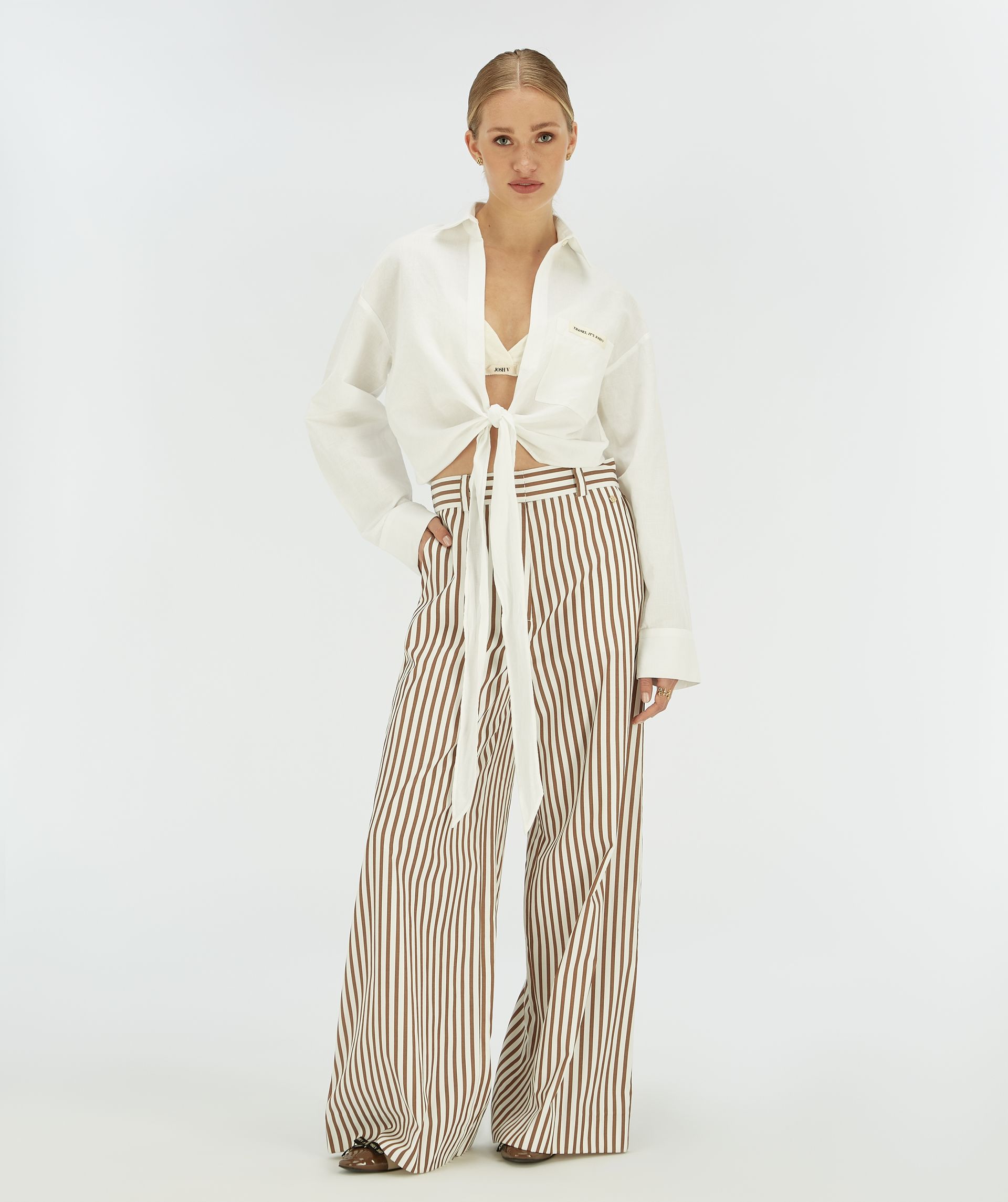 Model draagt een witte cropped blouse met striksluiting.