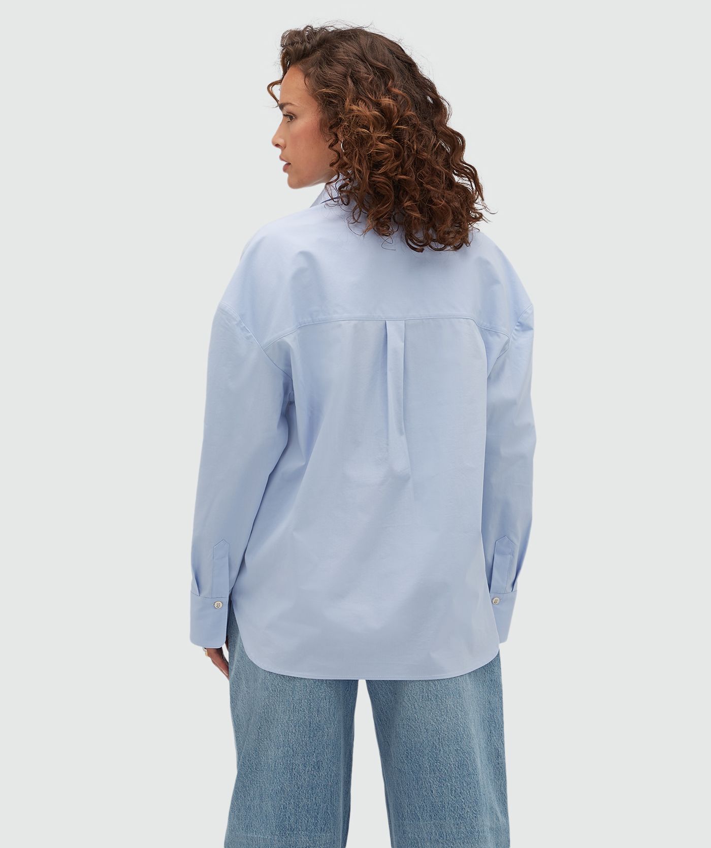 Achteraanzicht van een model in een lichtblauwe oversized blouse.