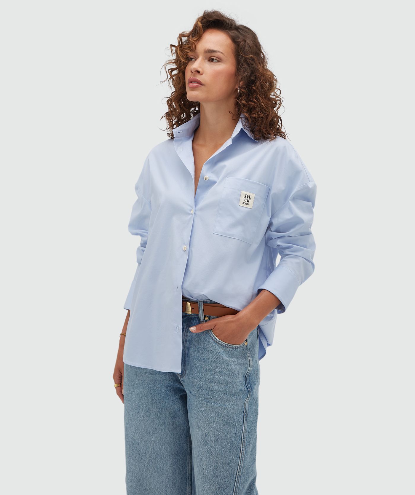 Model draagt een lichtblauwe oversized blouse met een borstzak voorzien van het JOSH V-logo.