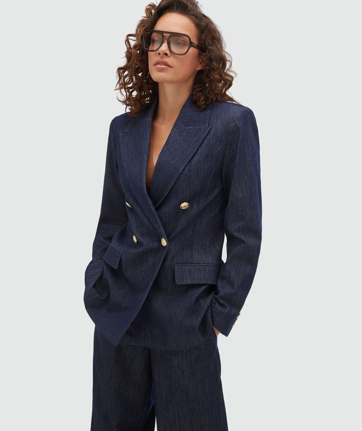 Model draagt een donkerblauwe blazer met gouden knopen aan de voorkant.