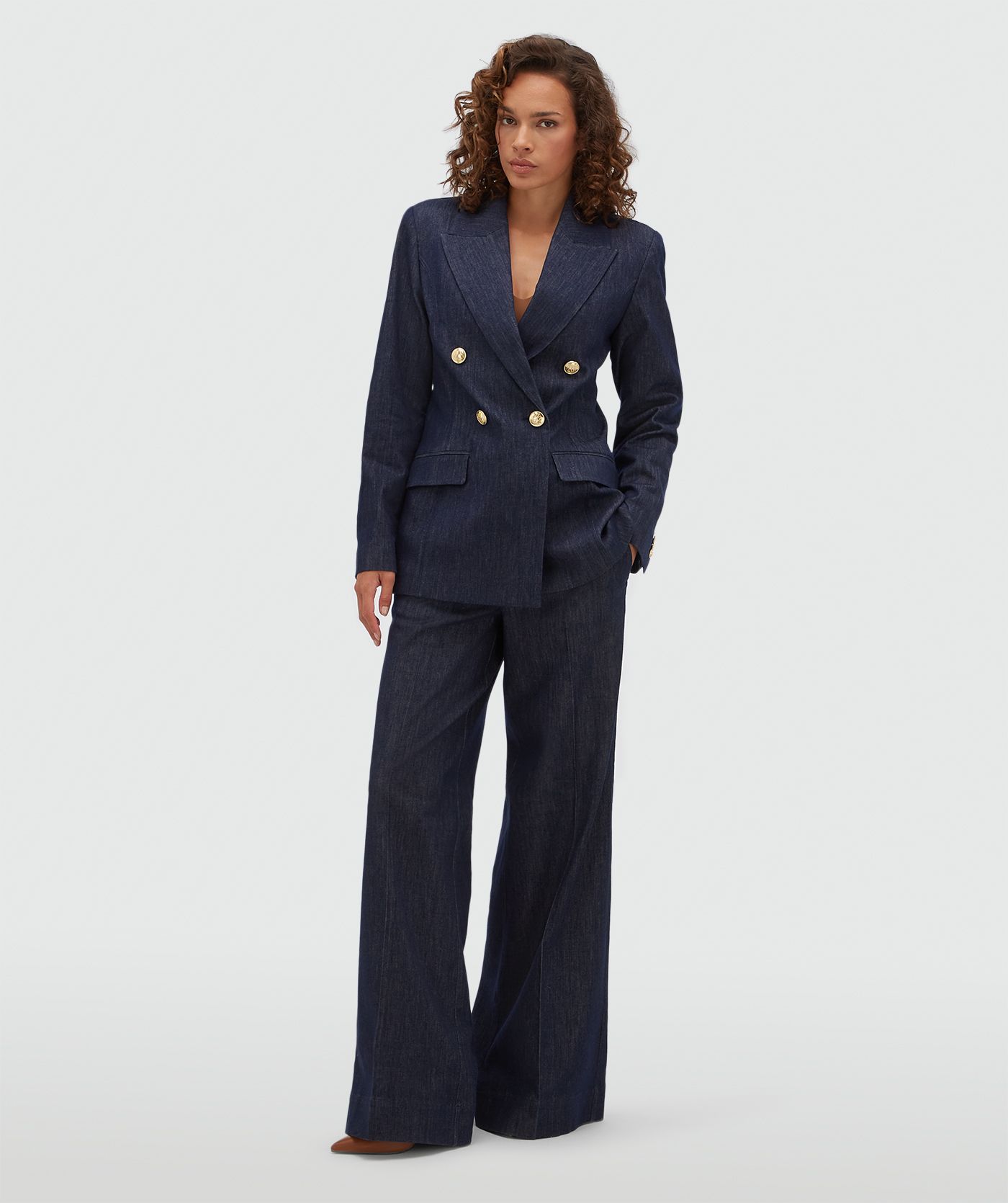 Model draagt een donkerblauwe blazer met gouden knopen aan de voorkant.