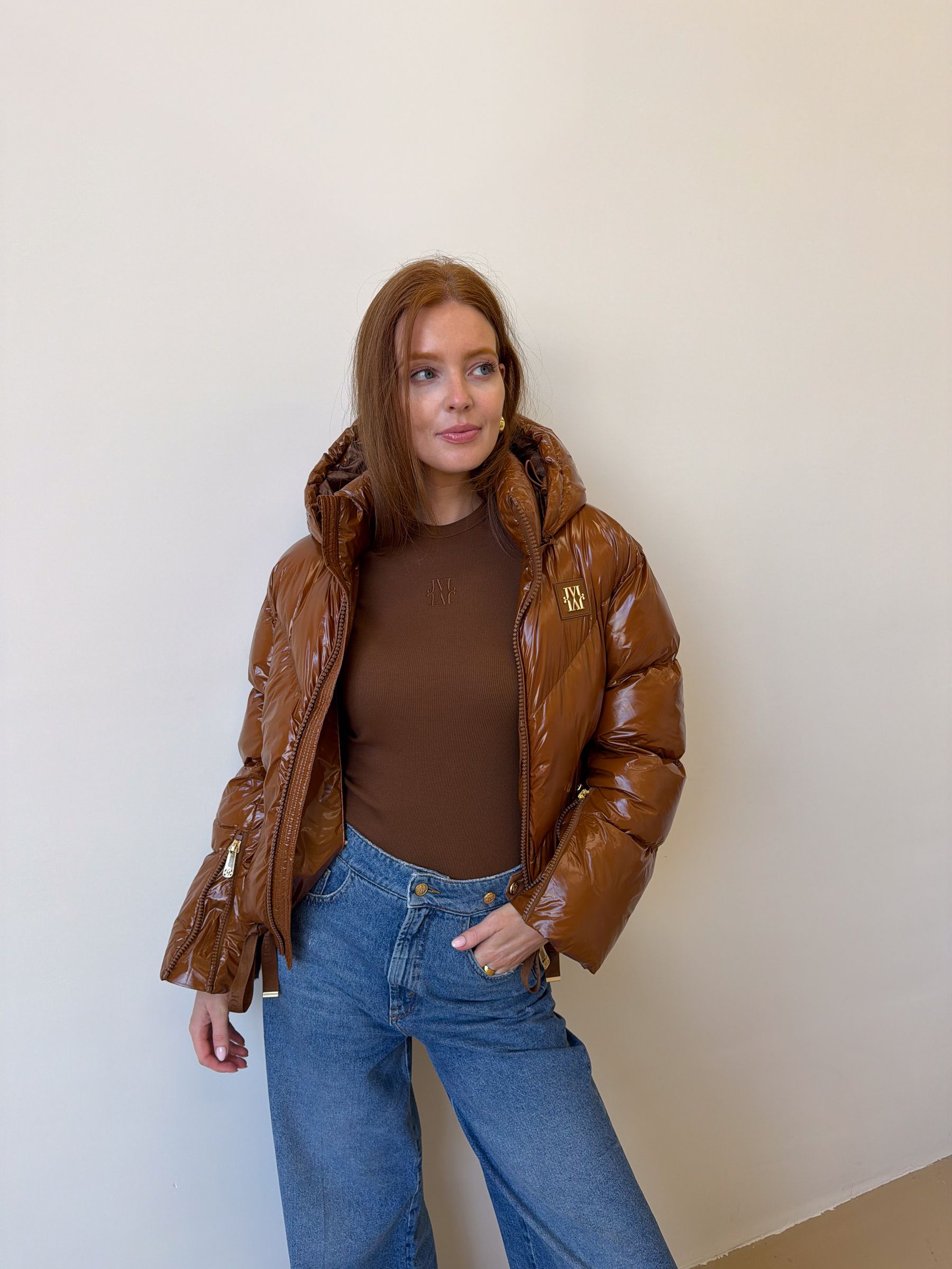 Model draagt een cognac kleurige lak look jas gecombineerd met een jeans.