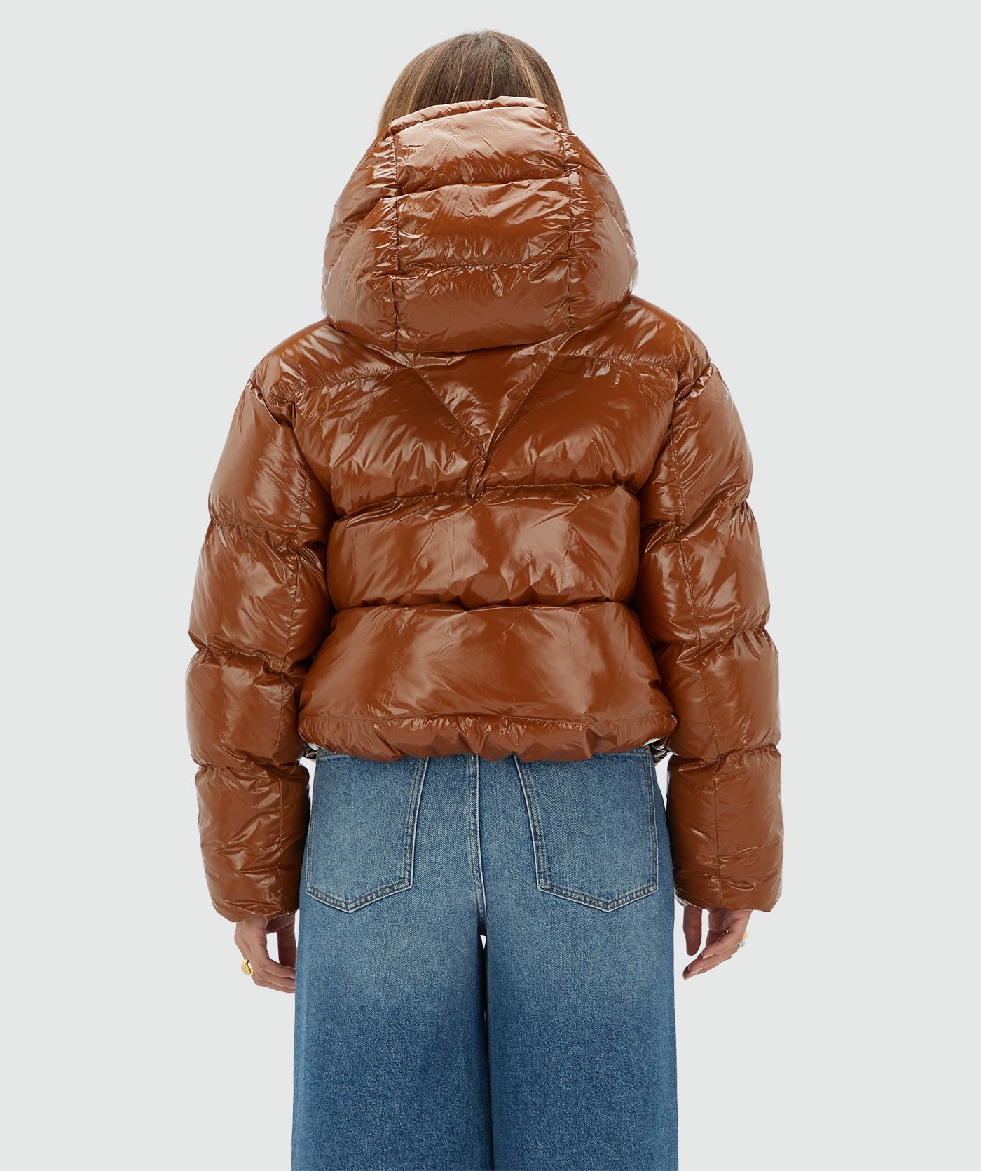 Model draagt een cognac kleurige lak look jas gecombineerd met een jeans.