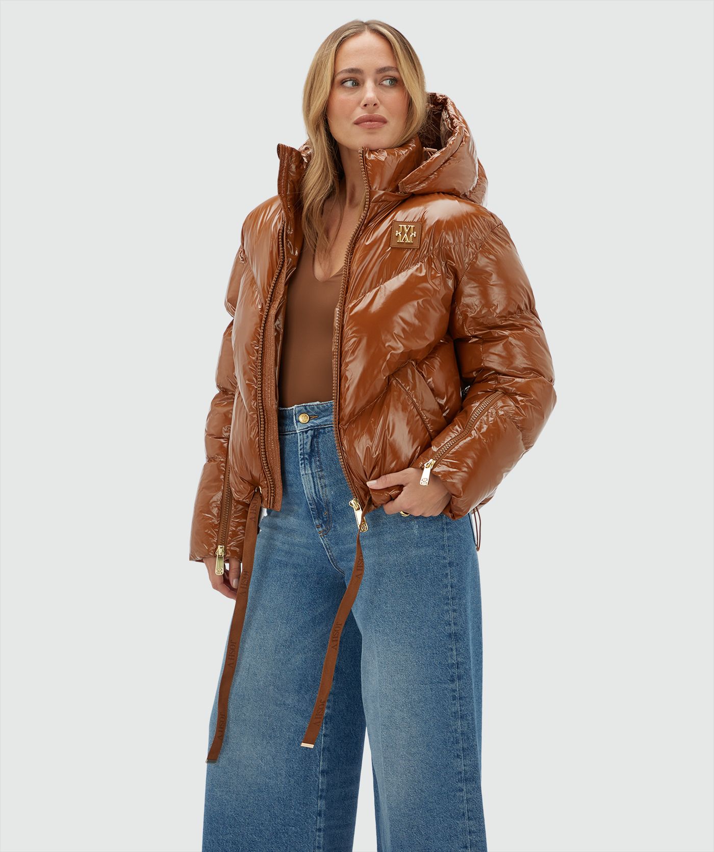 Model draagt een cognac kleurige lak look jas gecombineerd met een jeans.