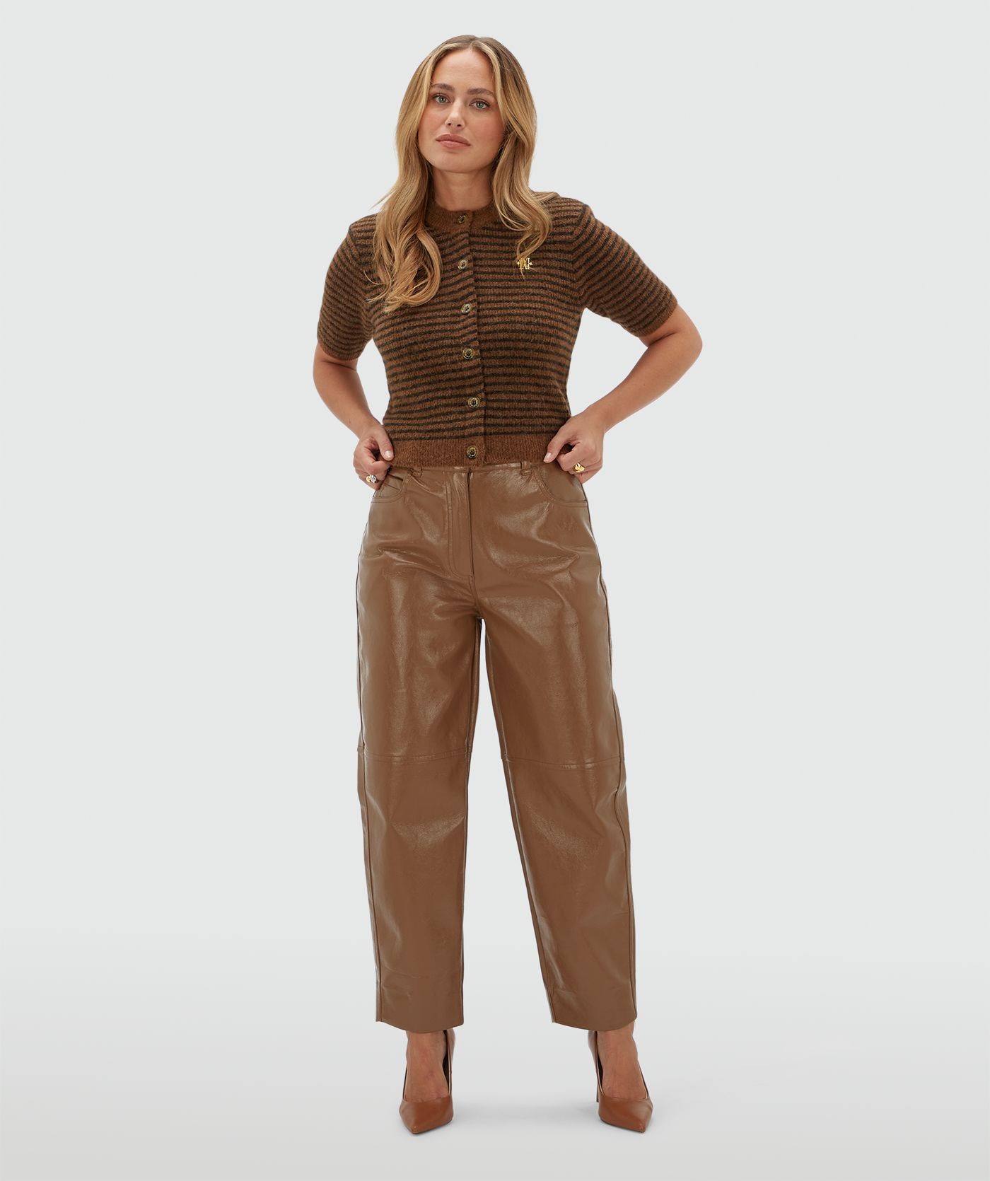 Model draagt een lichtbruin met donkerbruin gestreept vestje met korte mouwen gecombineerd op een lichtbruine lak look broek.