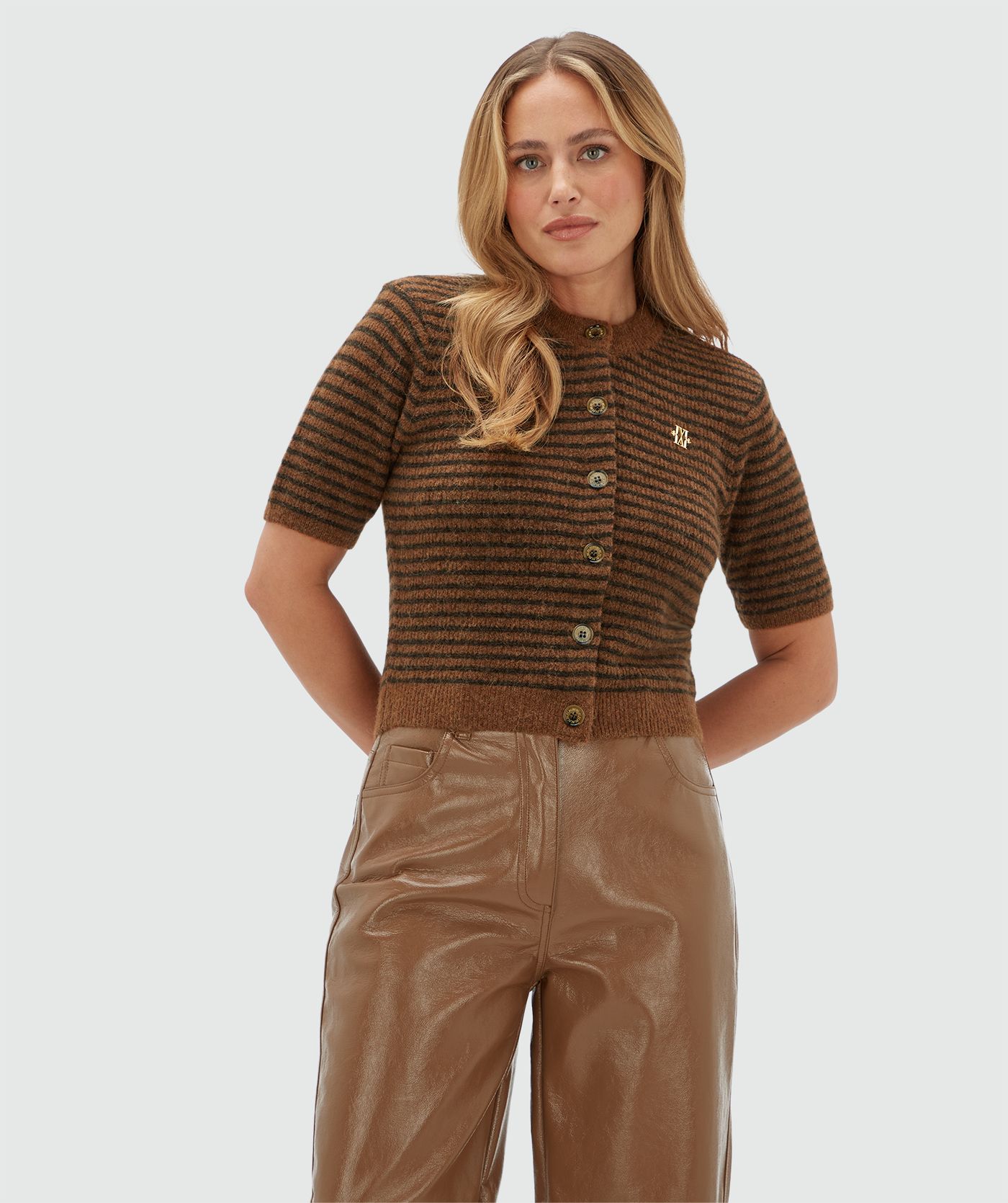 Model draagt een lichtbruin met donkerbruin gestreept vestje met korte mouwen gecombineerd op een lichtbruine lak look broek.