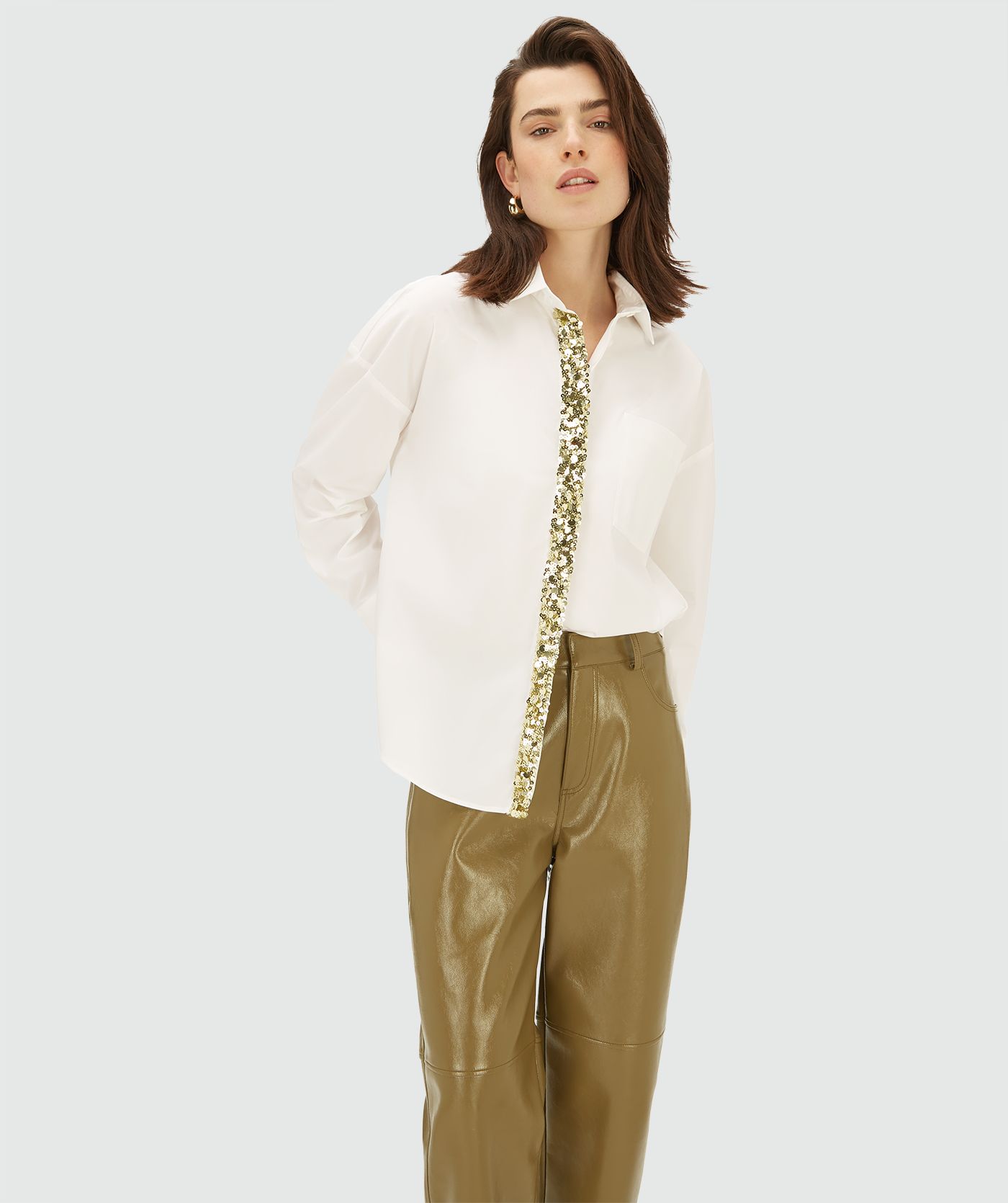 Model draagt een off witte blouse met een verticale strook goudkleurige strass-steentjes aan de voorzijde