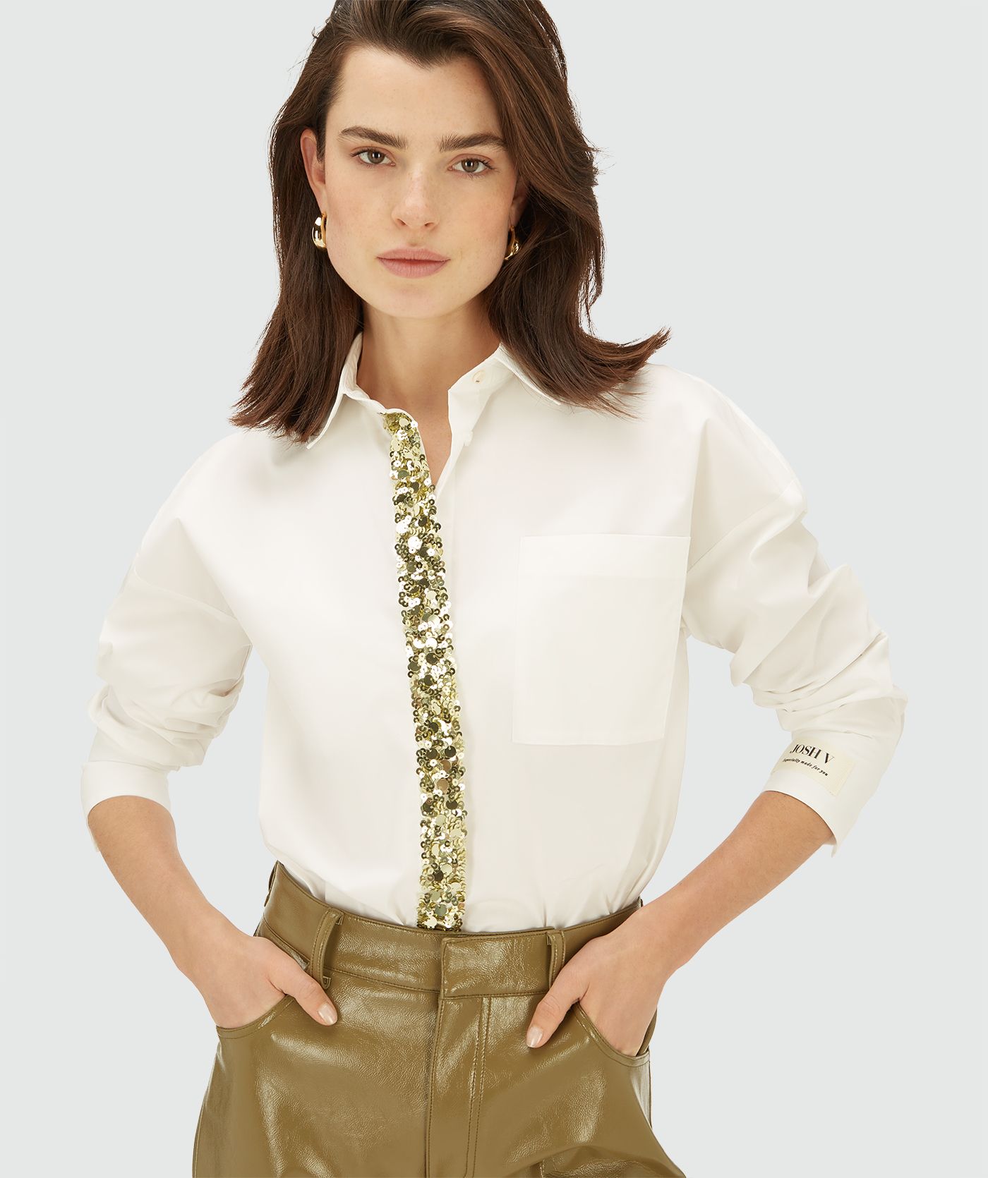 Model draagt een off witte blouse met een verticale strook goudkleurige strass-steentjes aan de voorzijde