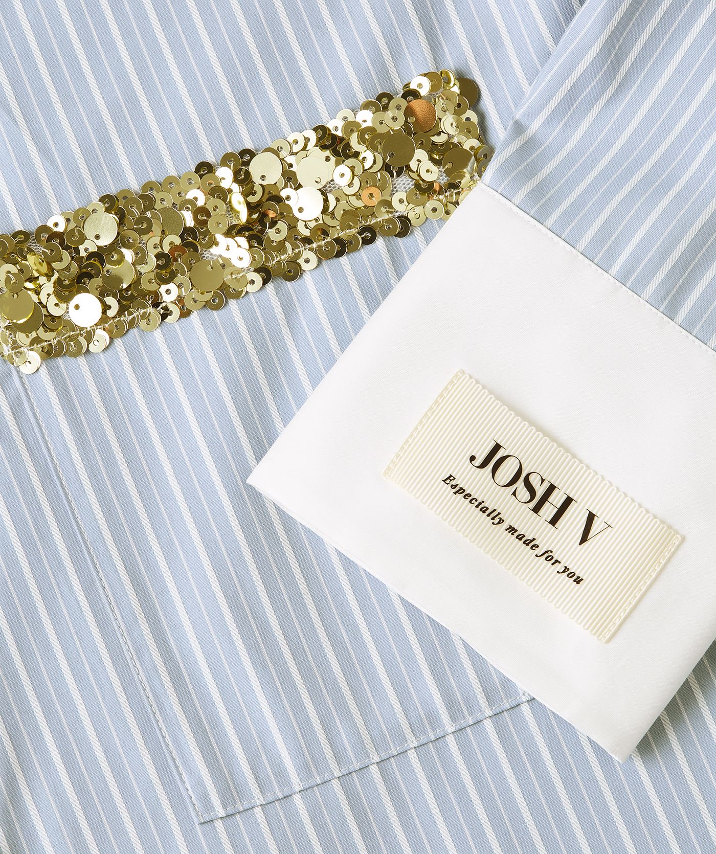 Close-up van het merklabel op de linkermouw en een borstzak afgewerkt met groen-gouden pailletten