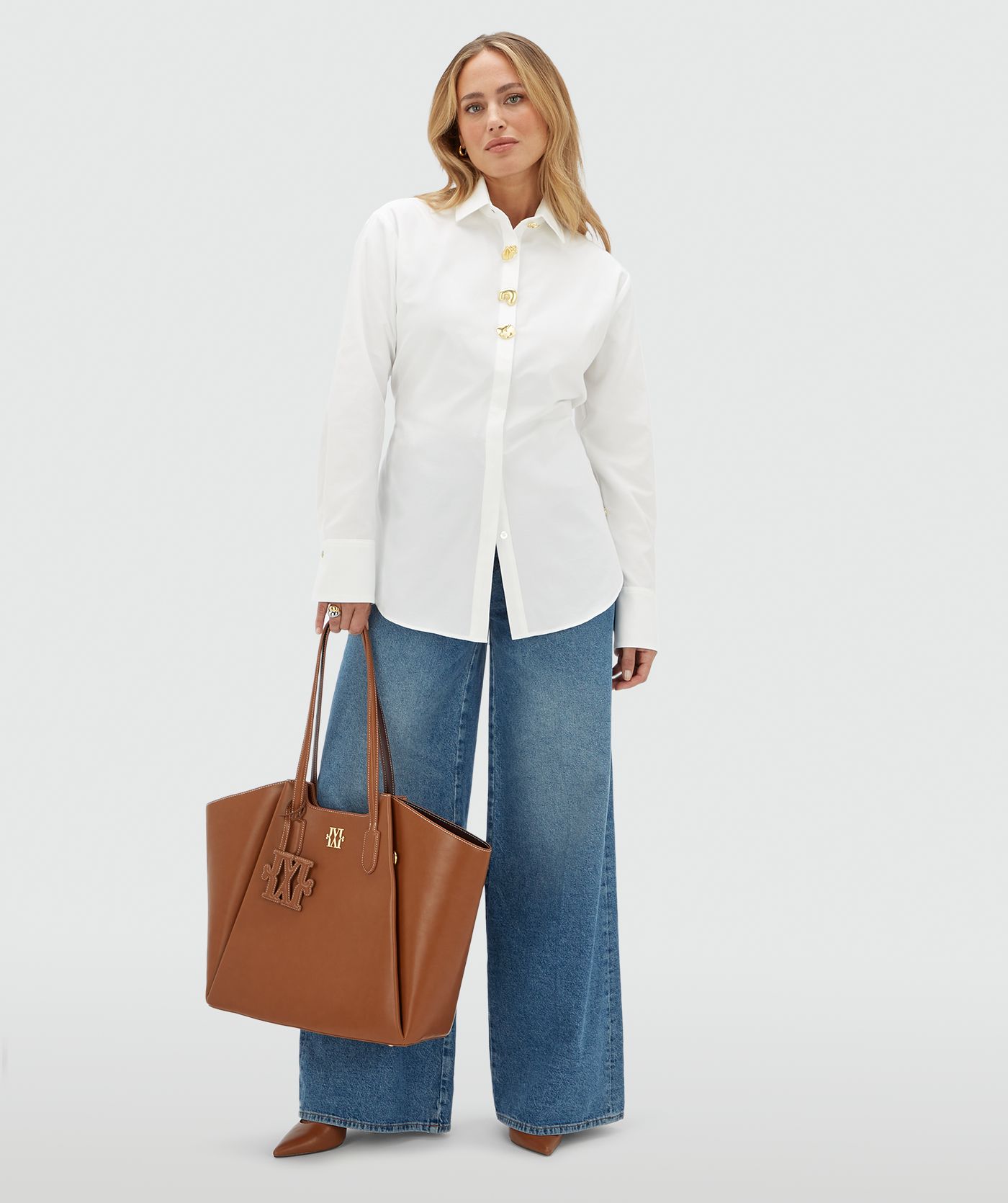 Model draagt een witte blouse aan de bovenkant vier gouden knopen. De blouse is gecombineerd op een jeans.