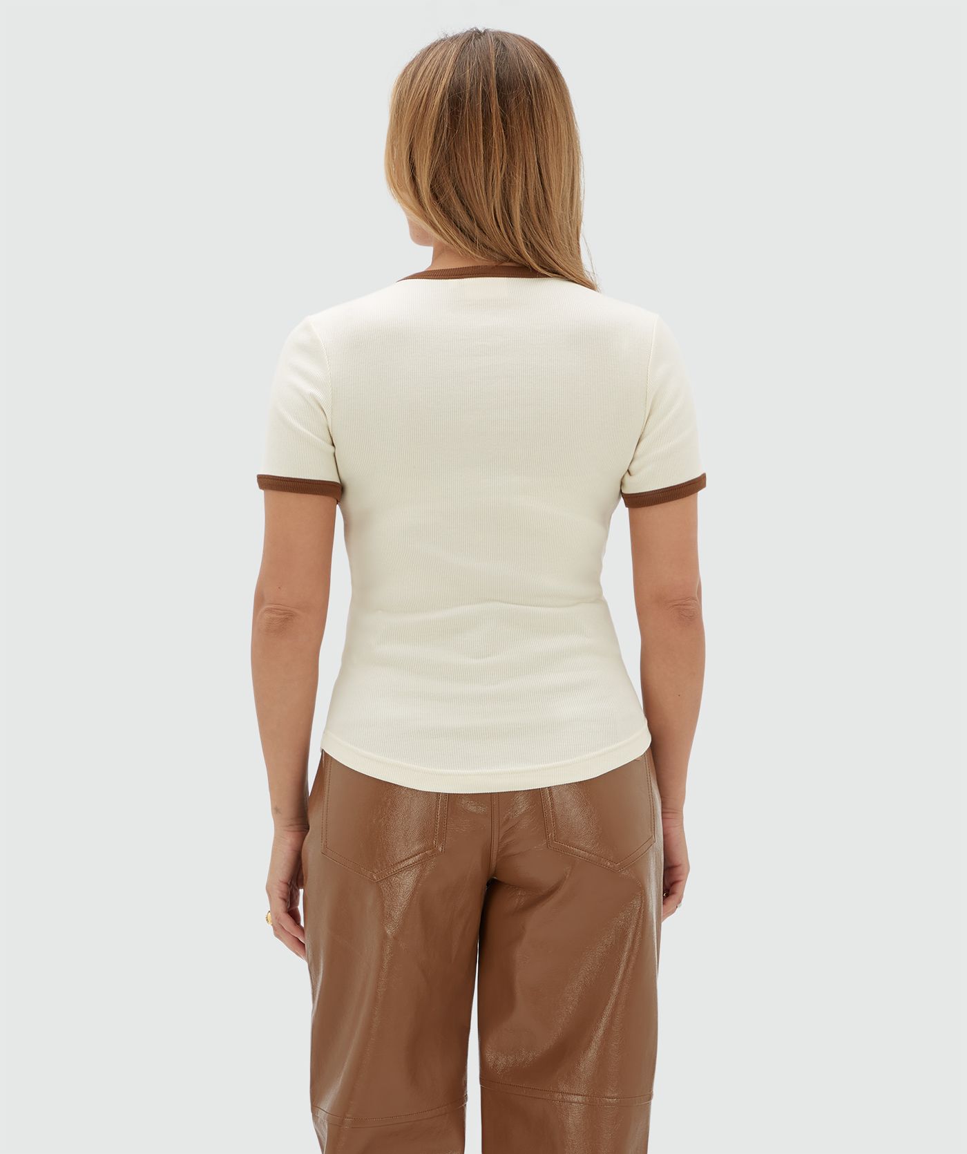 Achteraanzicht van een model in een wit T-shirt met een bruine halslijn en heeft ook bruine randjes bij de mouwen.