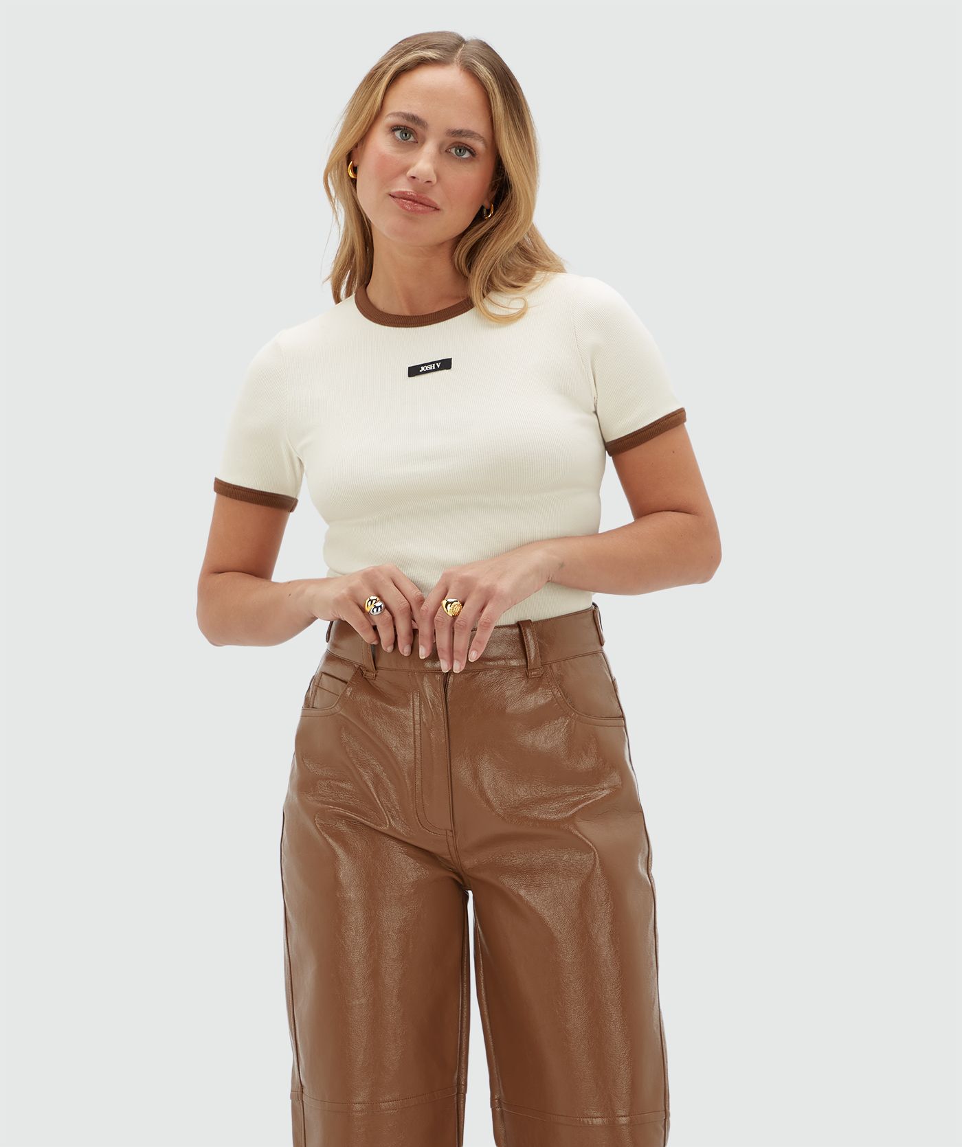 Model draagt een wit T-shirt met een JOSH V label aan de voorkant en heeft ook een bruine hals lijn en de randjes van de mouwen zijn ook bruin.