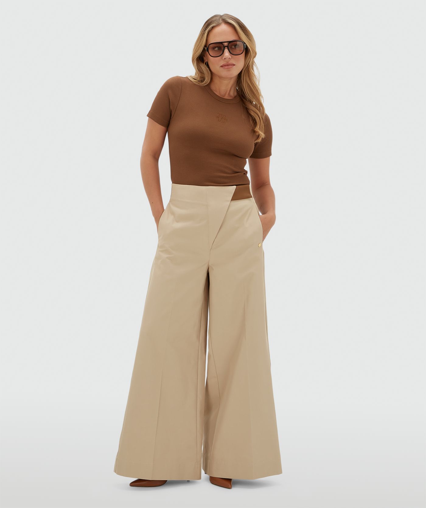 Model draagt een donkerbruin T-shirt met op de borst een JOSH V logo gecombineerd met een beige pantalon.