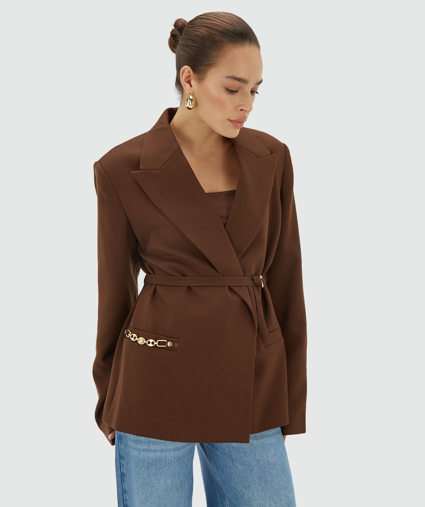 Model draagt een oversized Dark Brown blazer met schoudervullingen en is voorzien van een JOSH V branded chain op de steekzak en een riem met JOSH V branded haakjes - Josh V