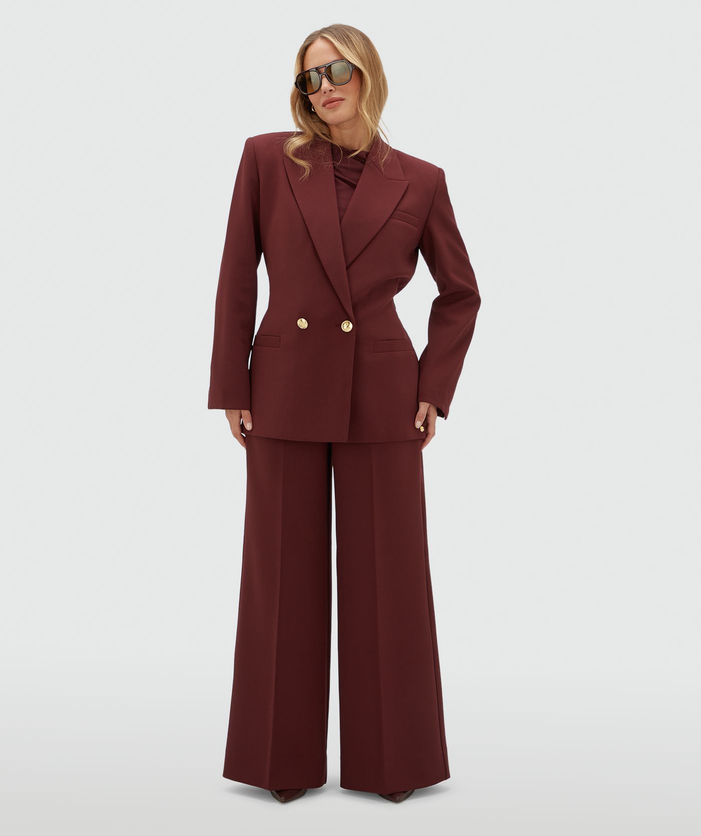 Model draagt een donkerrode blazer met een riempje achter zodat er meer taille gecreëerd kan worden. De blazer is gecombineerd met de bijpassende pantalon.