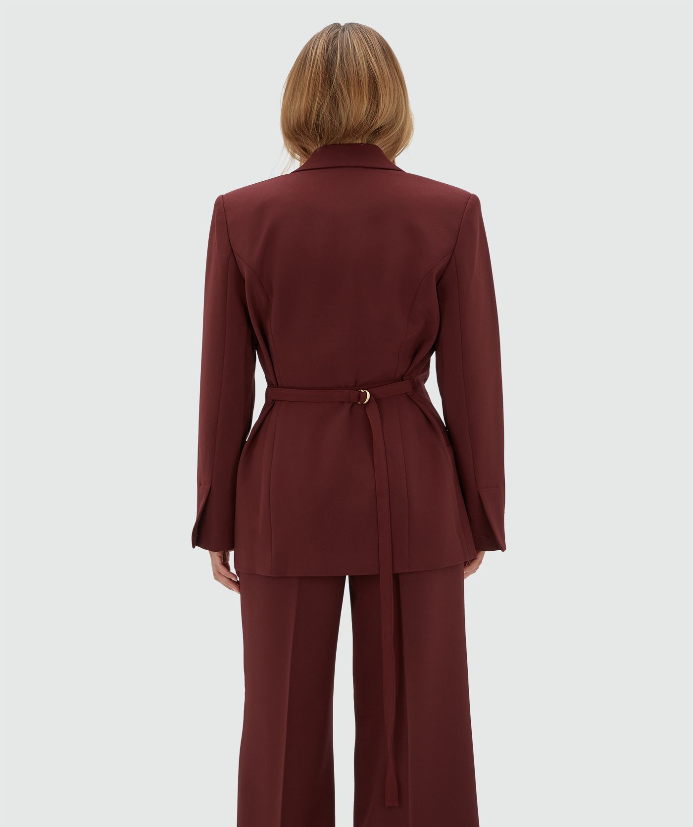 Achteraanzicht van een model in een donkerrode blazer met een riempje achter zodat er meer taille gecreëerd kan worden.