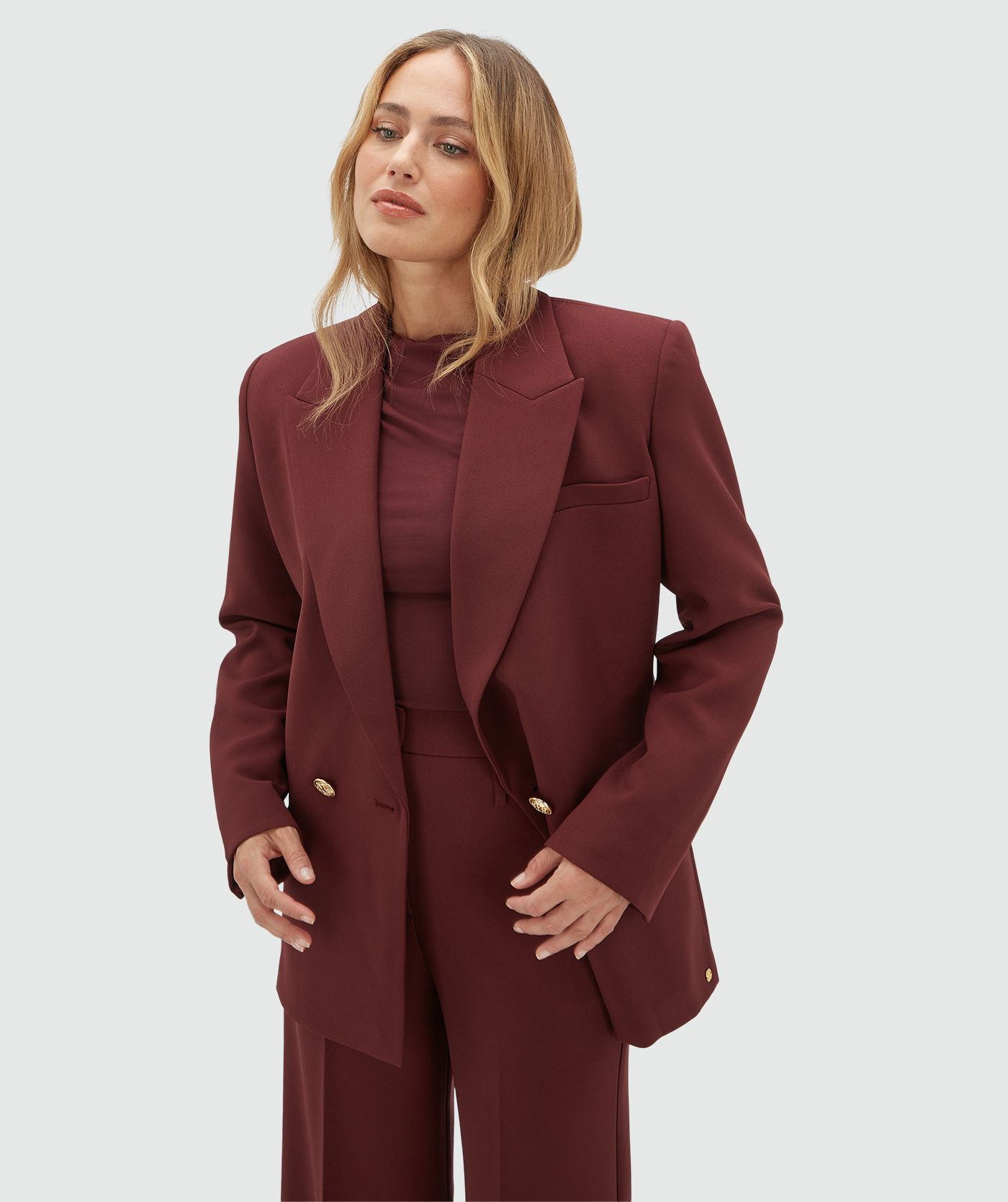 Model draagt een donkerrode blazer en draagt de blazer open.