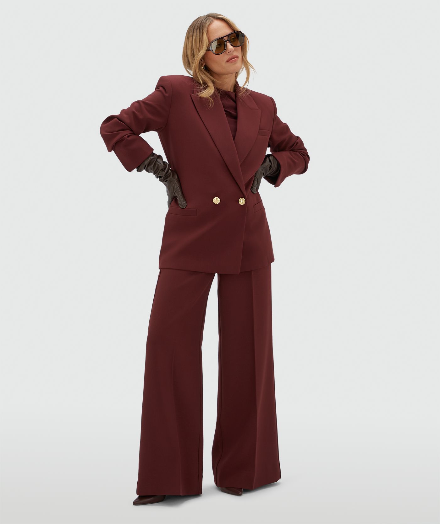 Model draagt een donkerrode blazer met een riempje achter zodat er meer taille gecreëerd kan worden. De blazer is gecombineerd met de bijpassende pantalon.