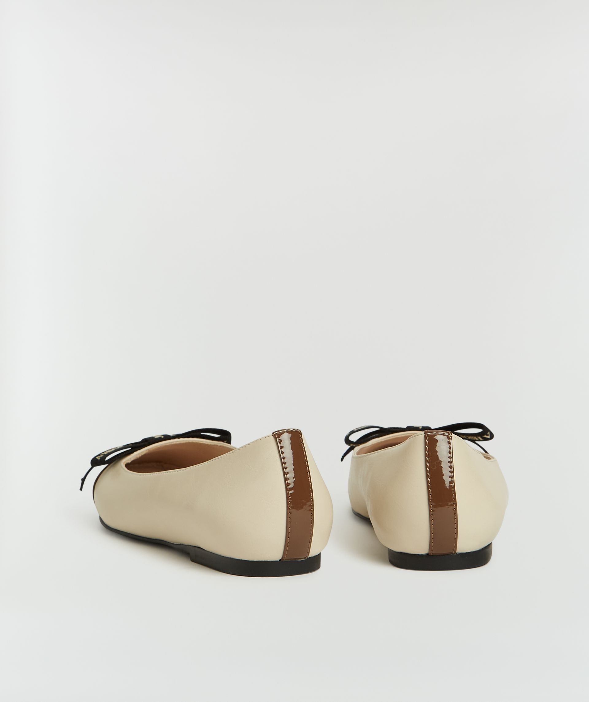 Achteraanzicht van ballerina's met beige en donkerbruin met strikje zonder model, weergegeven op een lichtgrijze achtergrond.