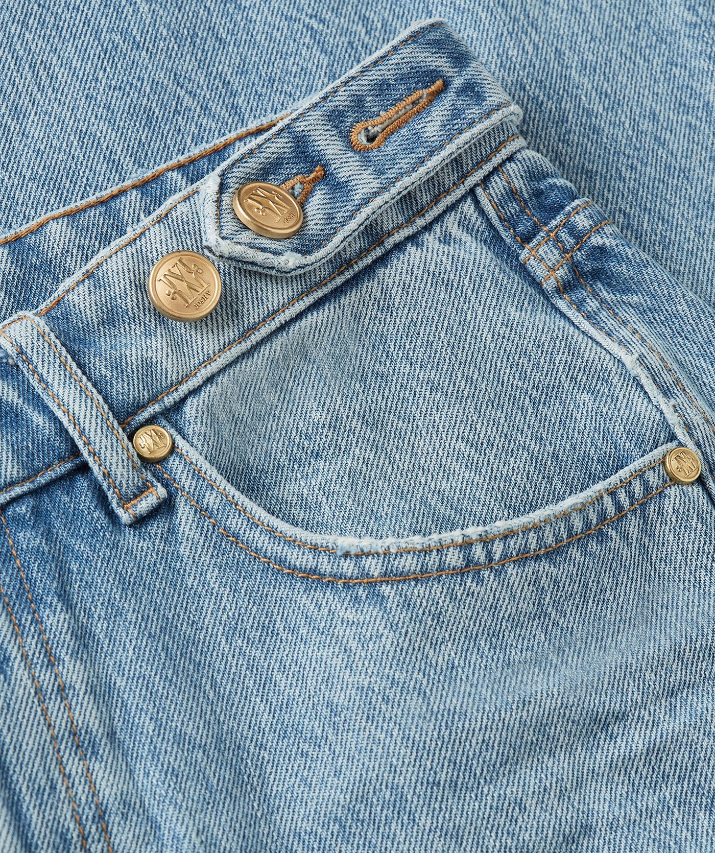 Close-up van lichtblauwe denim jeans met JV knoopdetails. 