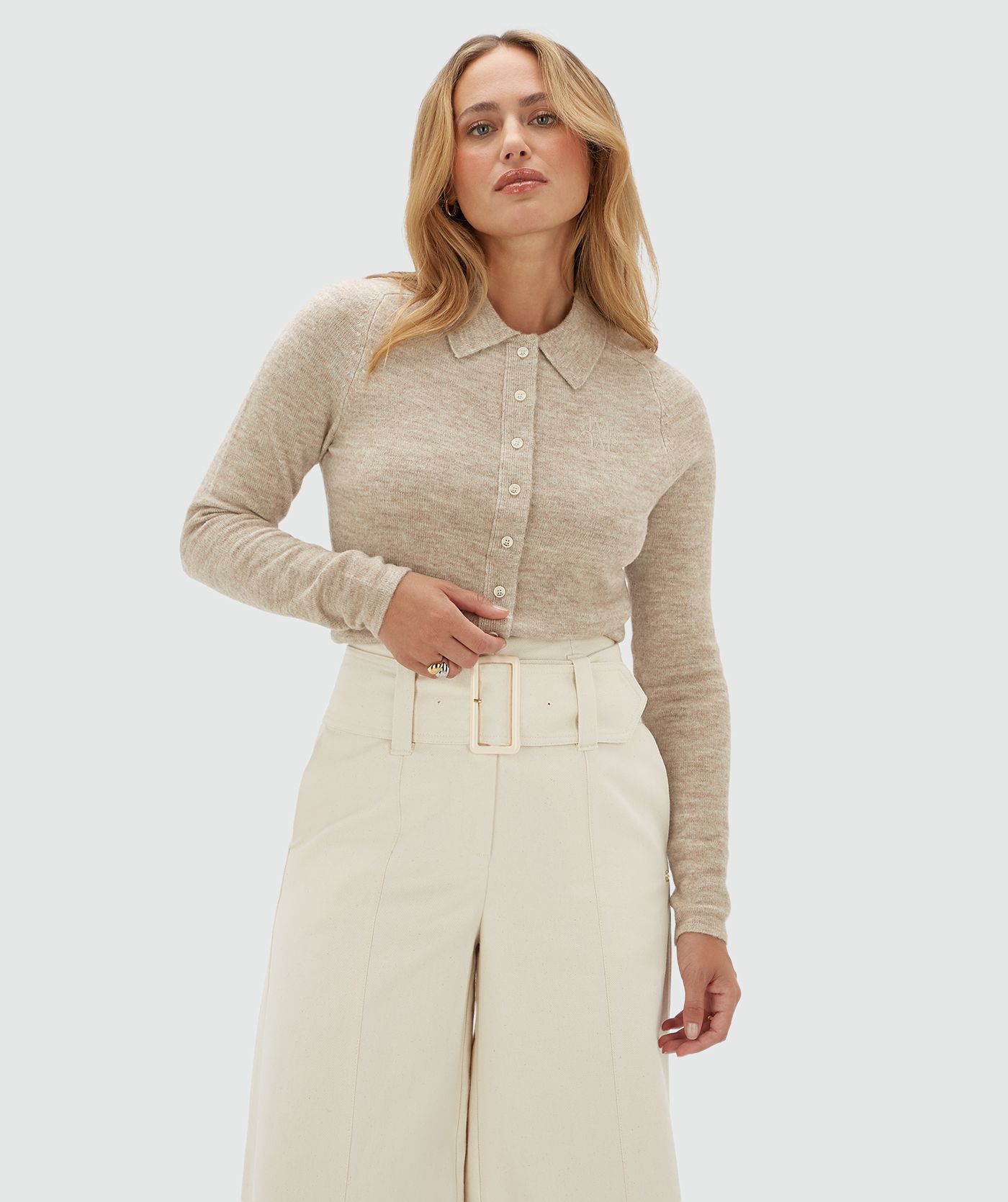 Model draagt een beige vestje met kraag en witte knoopjes gecombineerd op een gebroken witte broek.