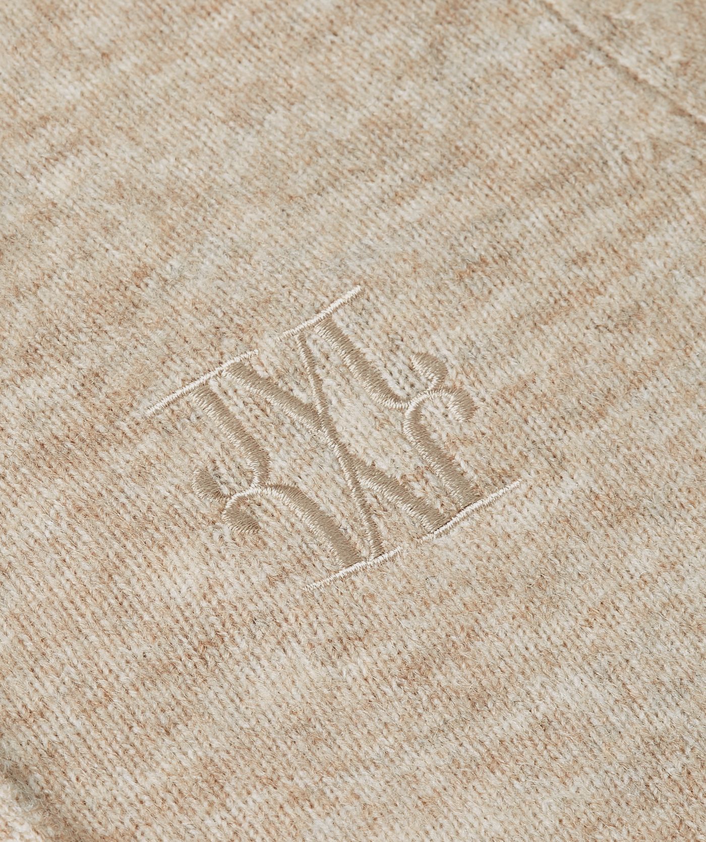 Close-up van het logo op de borst van het beige vestje. 