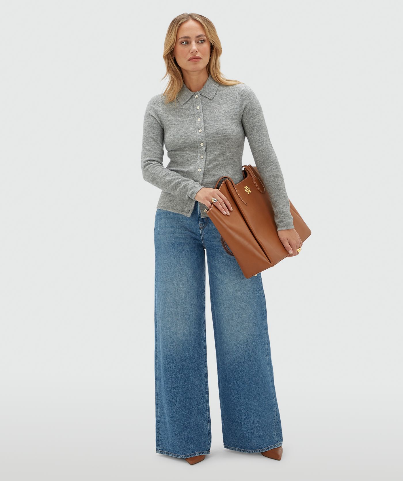 Model draagt een grijs vestje met witte knoopjes en een kraag op een jeans.