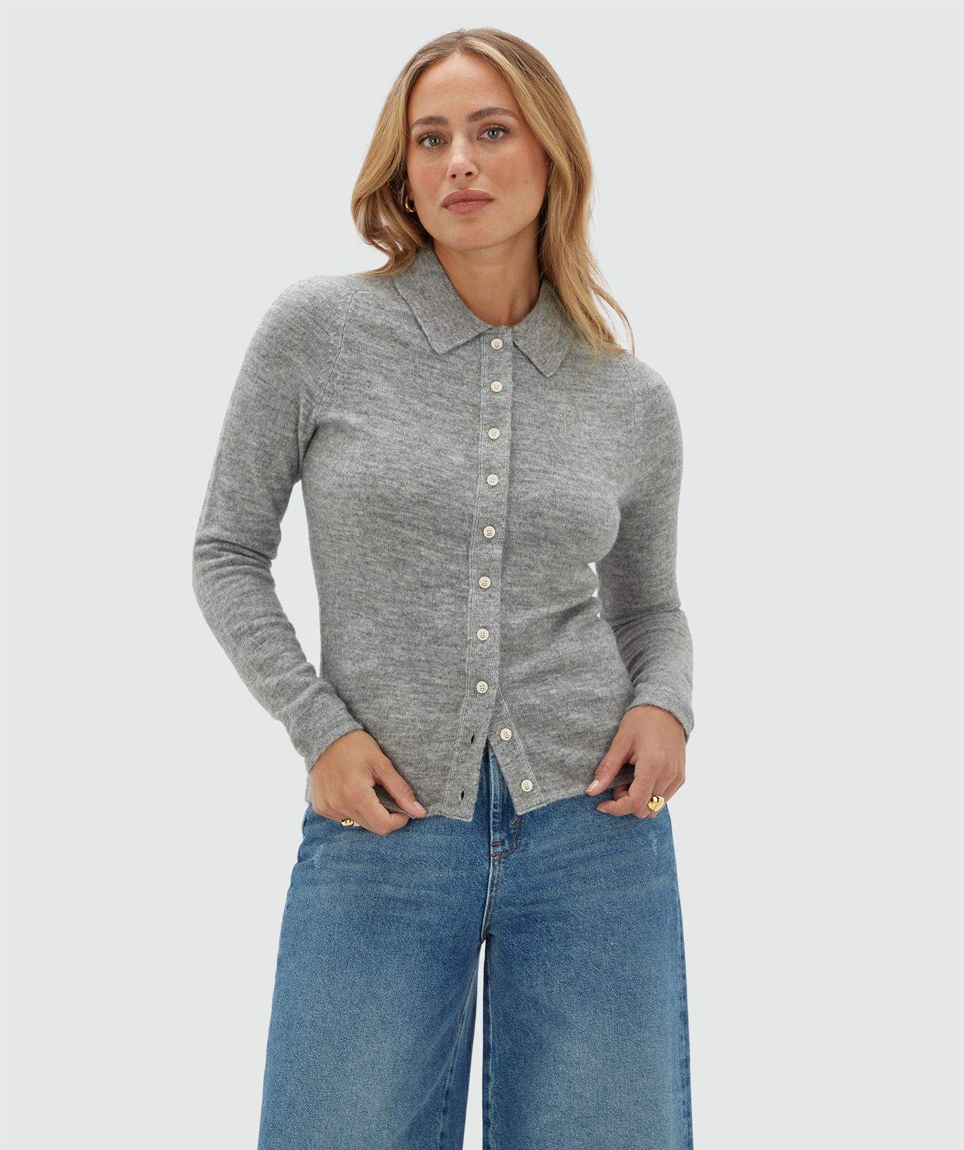 Model draagt een grijs vestje met witte knoopjes en een kraag op een jeans.
