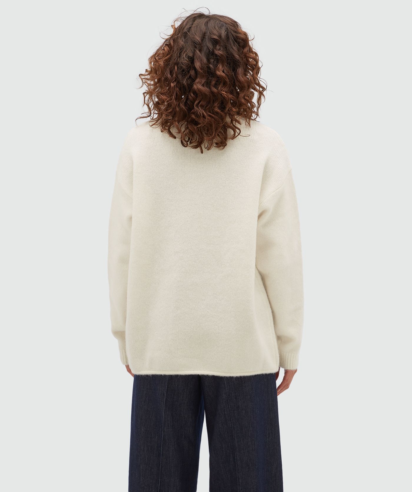 Achteraanzicht van een model in een oversized gebroken witte trui.