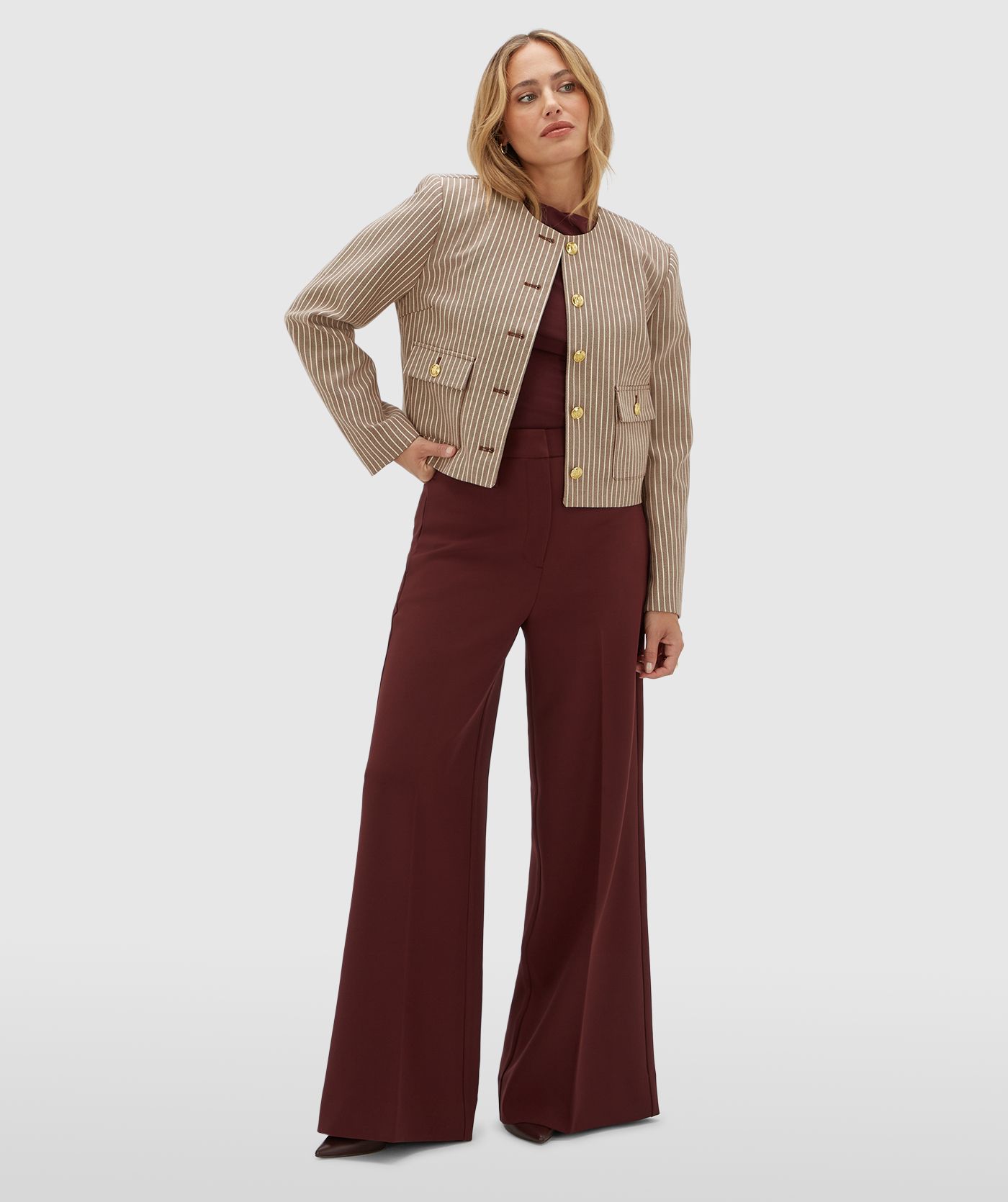 Model draagt een donkerrood met wit gestreept jasje met gouden knopen. Het jasje is gecombineerd met een donkerrode pantalon.