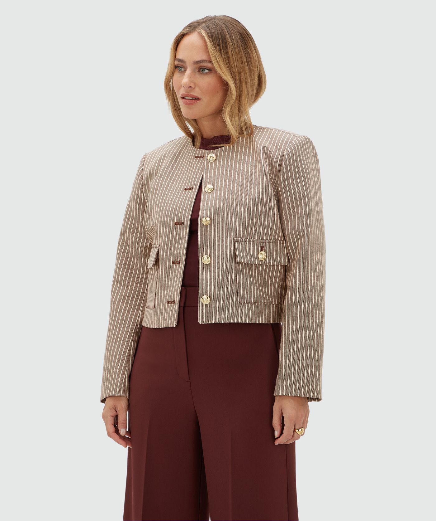 Model draagt een donkerrood met wit gestreept jasje met gouden knopen. Het jasje is gecombineerd met een donkerrode pantalon.