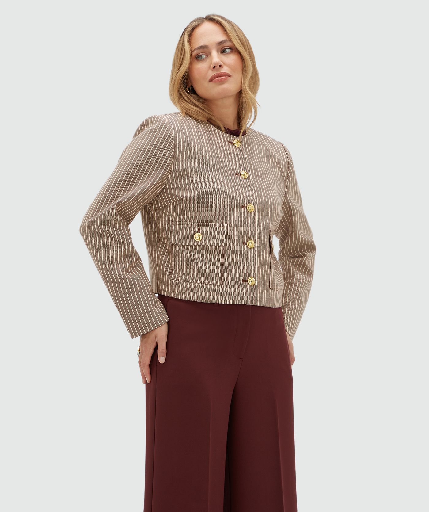Model draagt een donkerrood met wit gestreept jasje met gouden knopen. Het jasje is gecombineerd met een donkerrode pantalon.