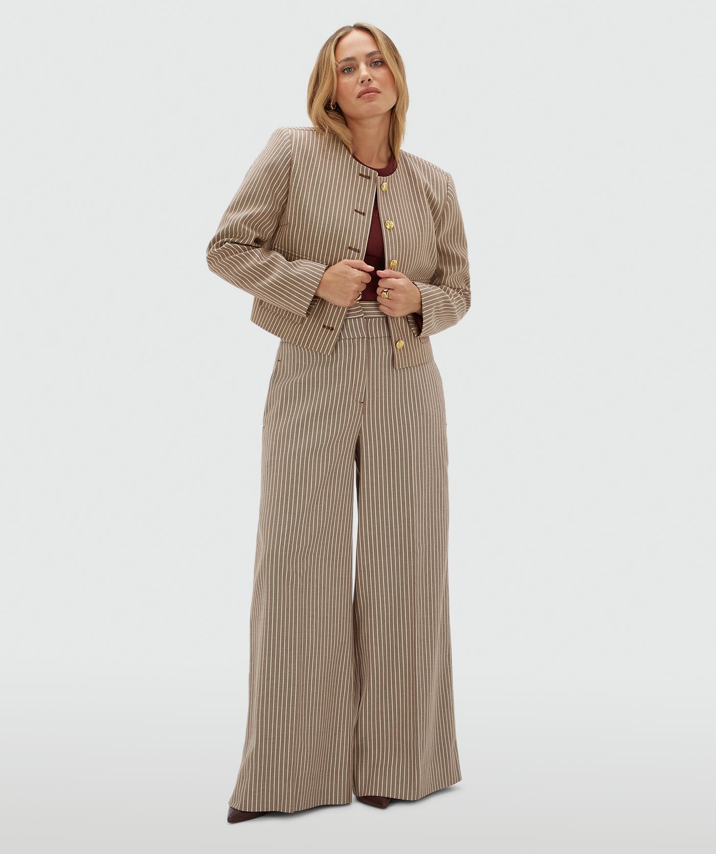 Model draagt een donkerrood met wit gestreept jasje met gouden knopen. Het model draagt het jasje samen met de bijpassende pantalon. 