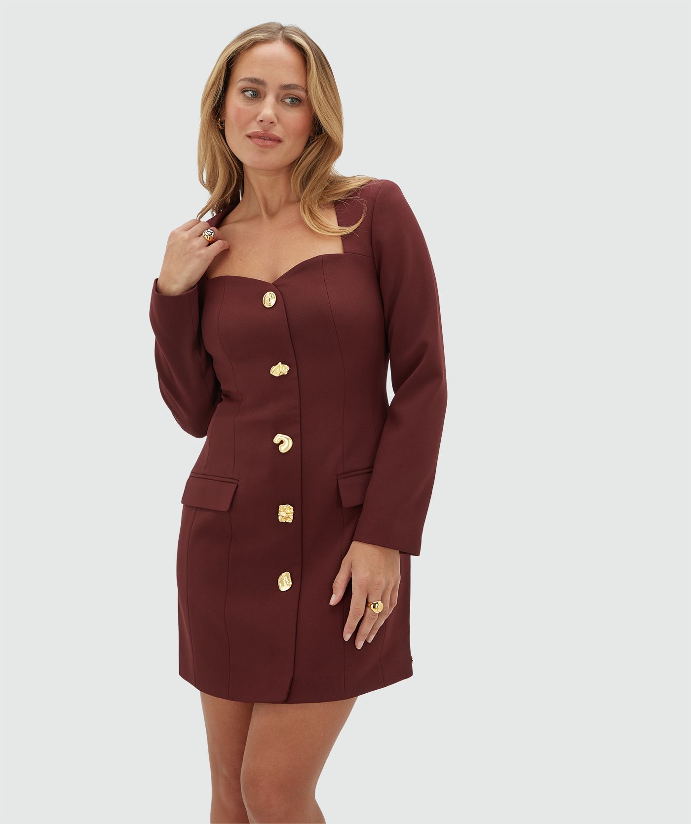 Model draagt een donkerrood jurkje met gouden knopen aan de voorkant. het jurkje heeft ook een hartvormige halslijn.