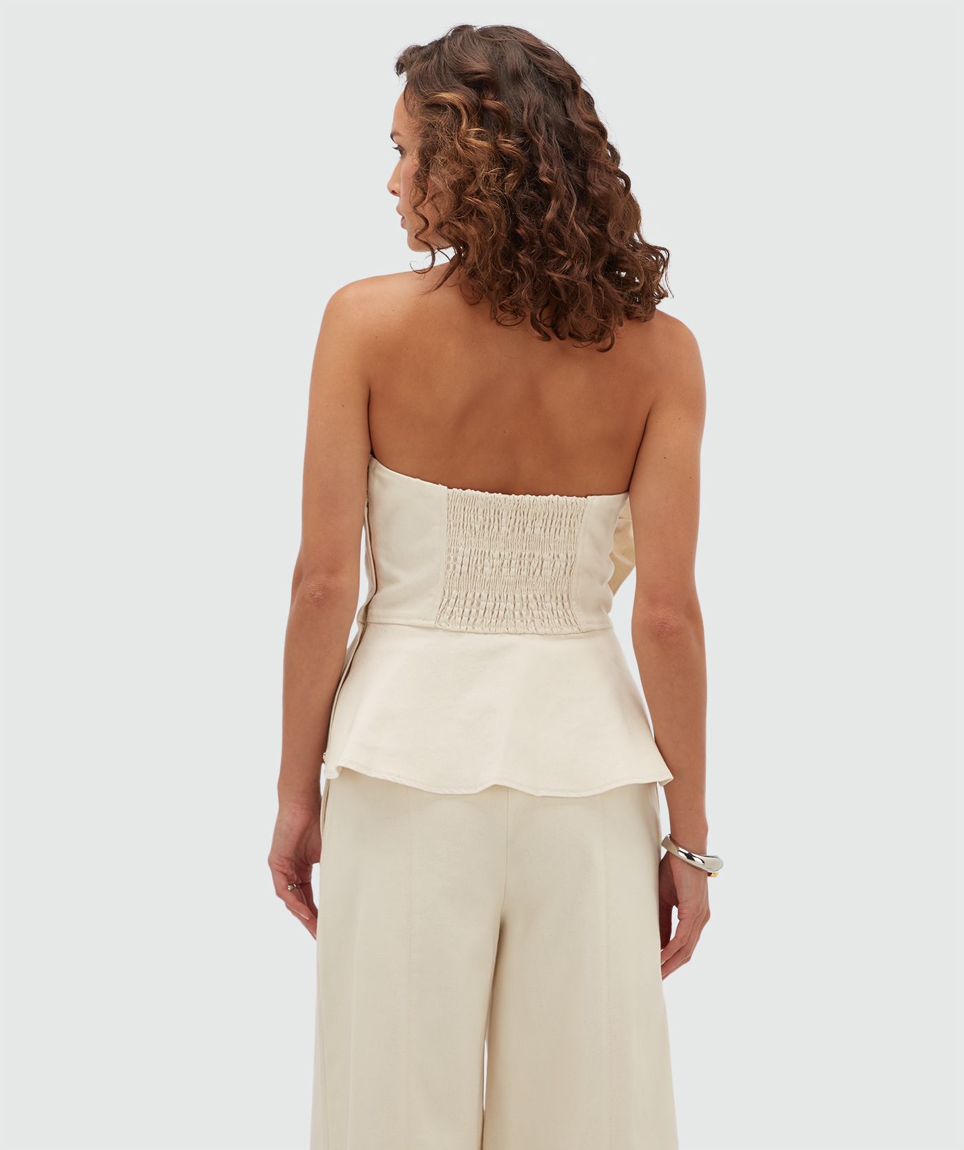 Achteraanzicht van een model in een gebroken witte bustier top met elastiek aan de achterkant.