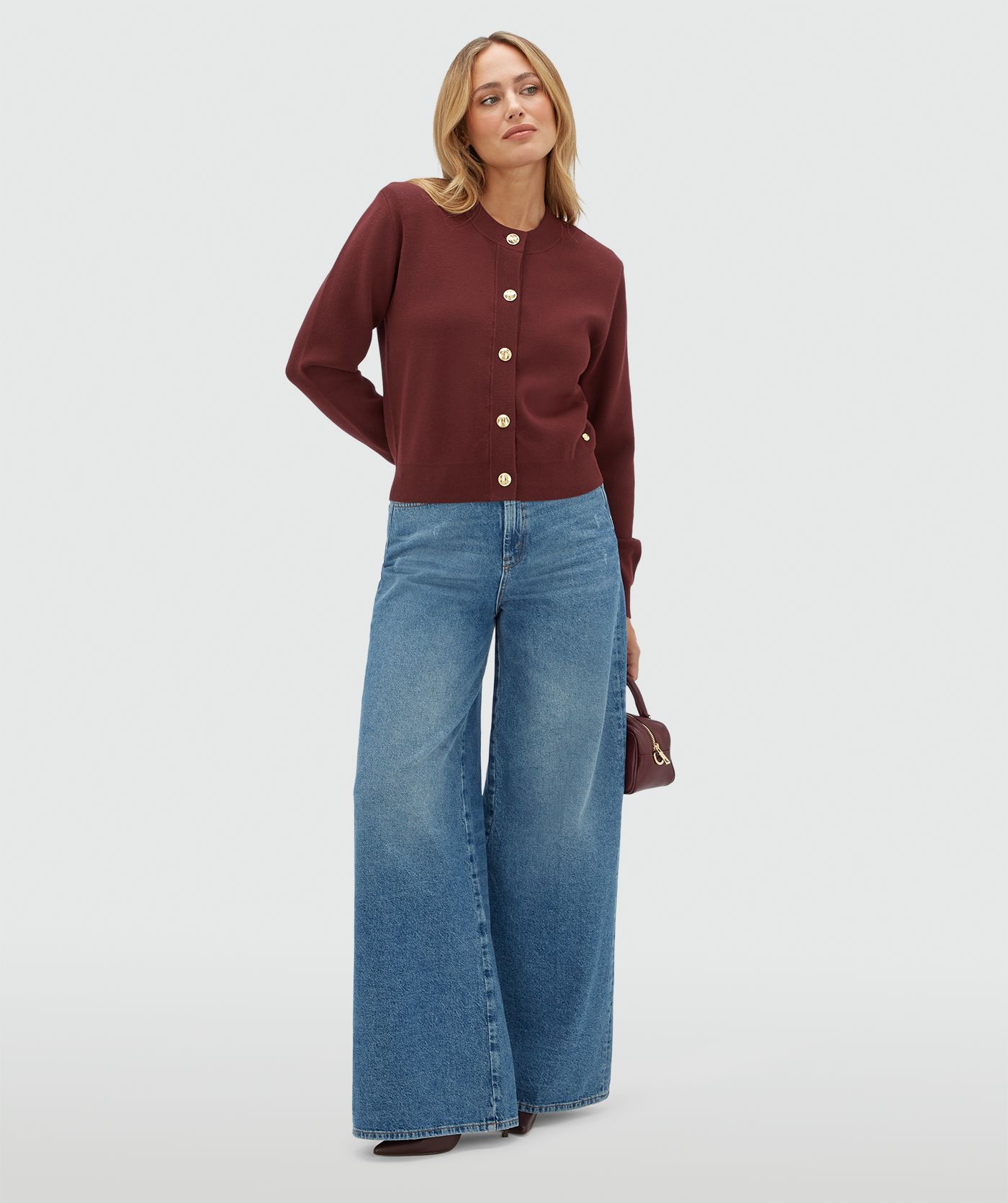 Model draagt een donkerrood vest met gouden knopen en schoudervullingen gecombineerd met een jeans.