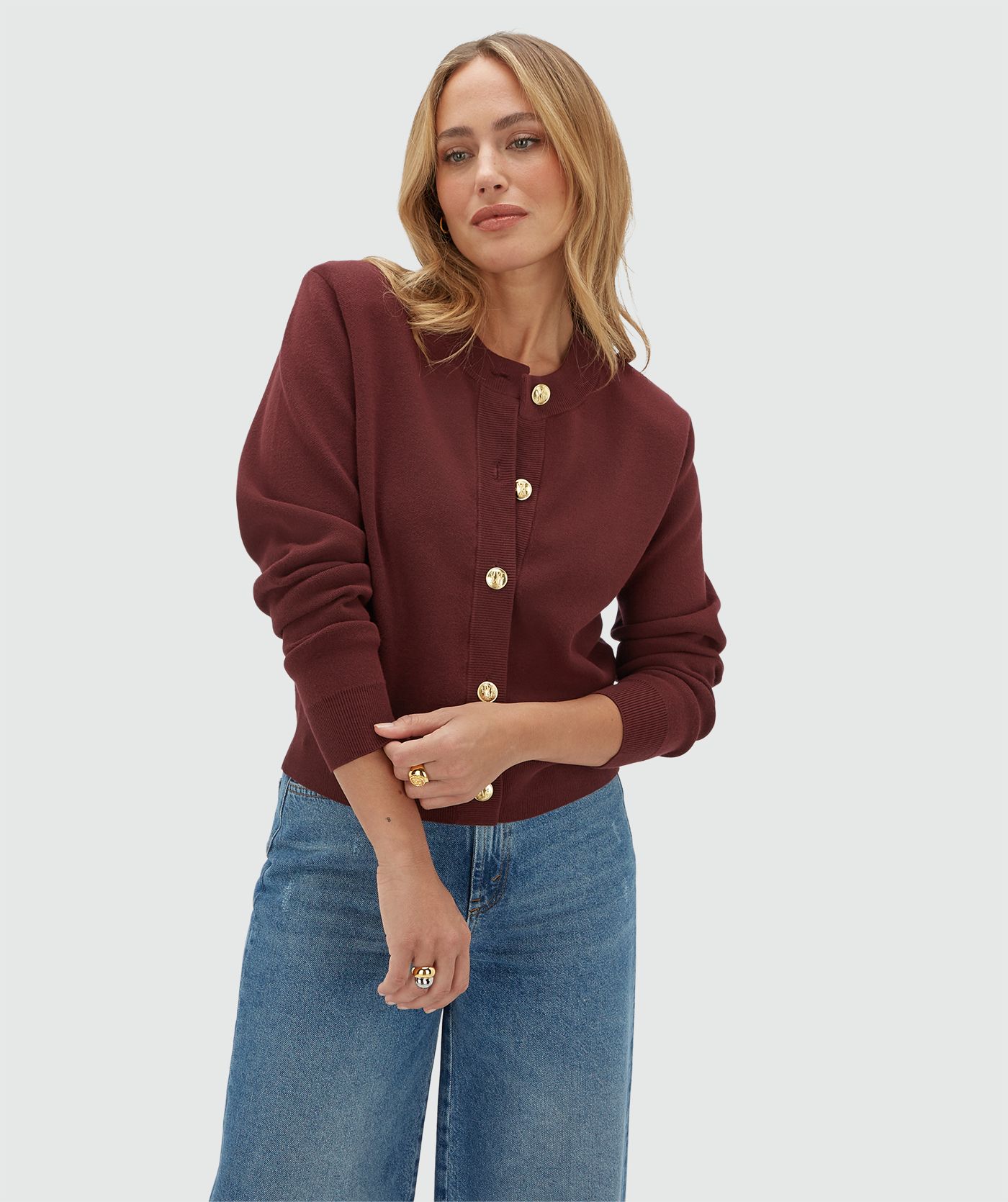 Model draagt een donkerrood vest met gouden knopen en schoudervullingen gecombineerd met een jeans.