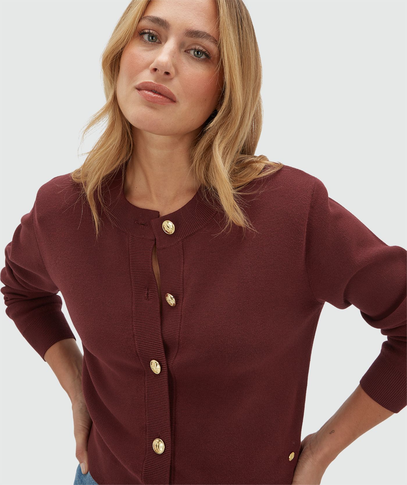 Model draagt een donkerrood vest met gouden knopen en schoudervullingen gecombineerd met een jeans.