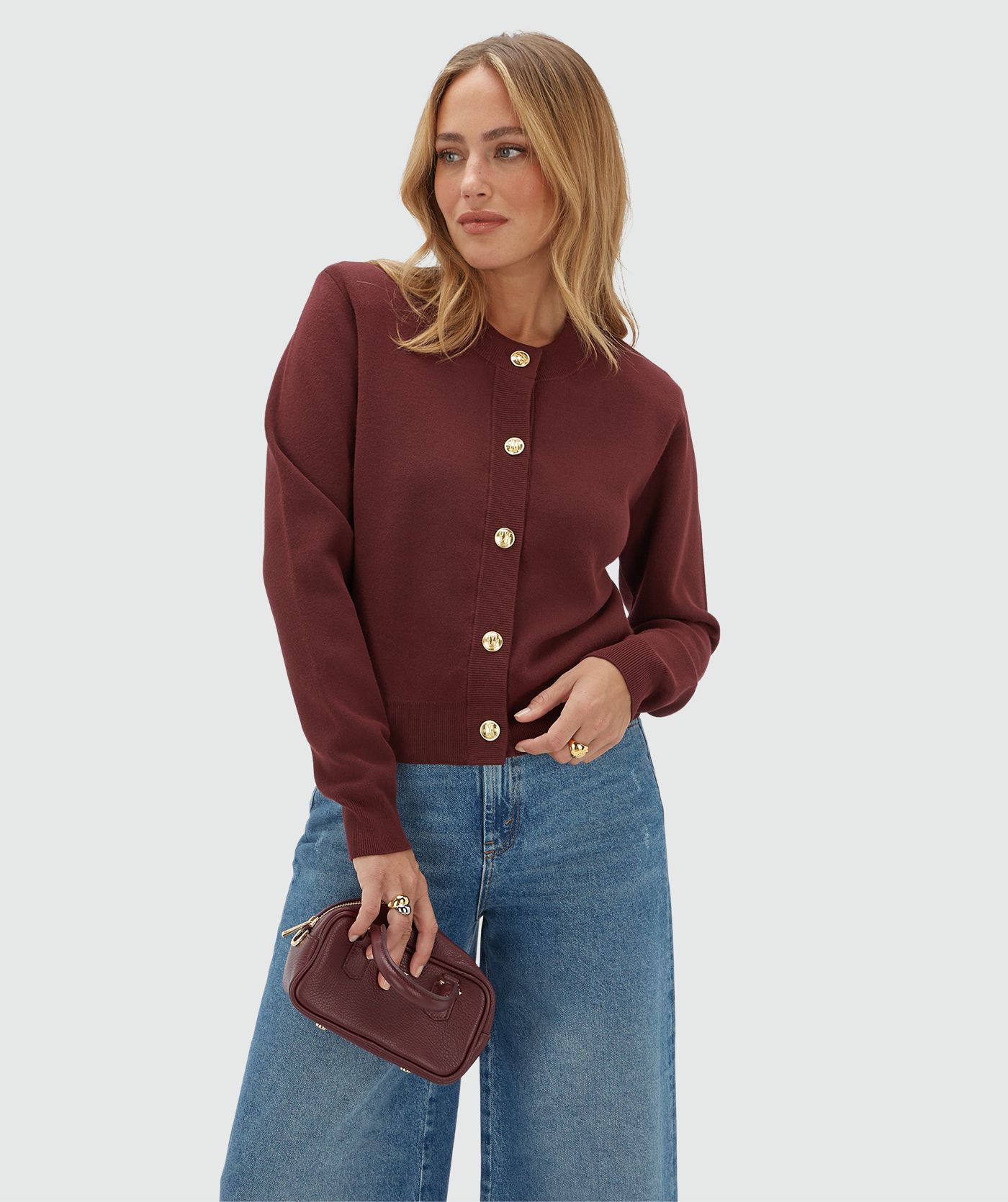 Model draagt een donkerrood vest met gouden knopen en schoudervullingen gecombineerd met een jeans.
