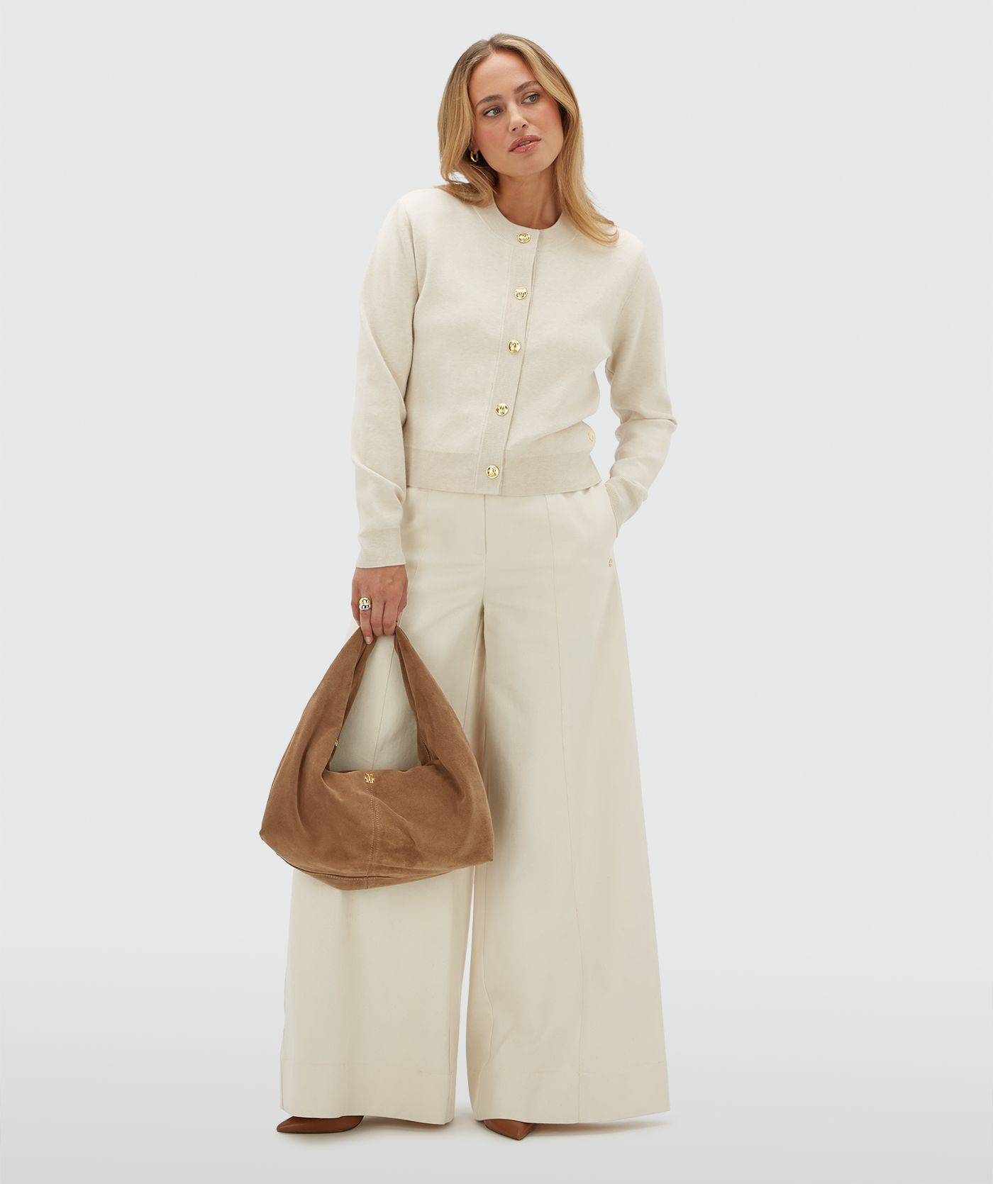 Model draagt een gebroken wit vest met gouden knopen en schoudervullingen op een beige broek.