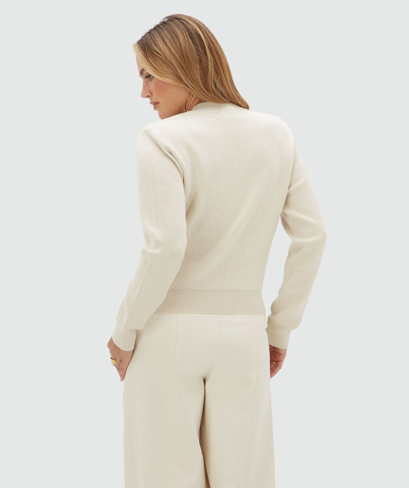 Achteraanzicht van een model in een gebroken wit vest gecombineerd met een beige broek.
