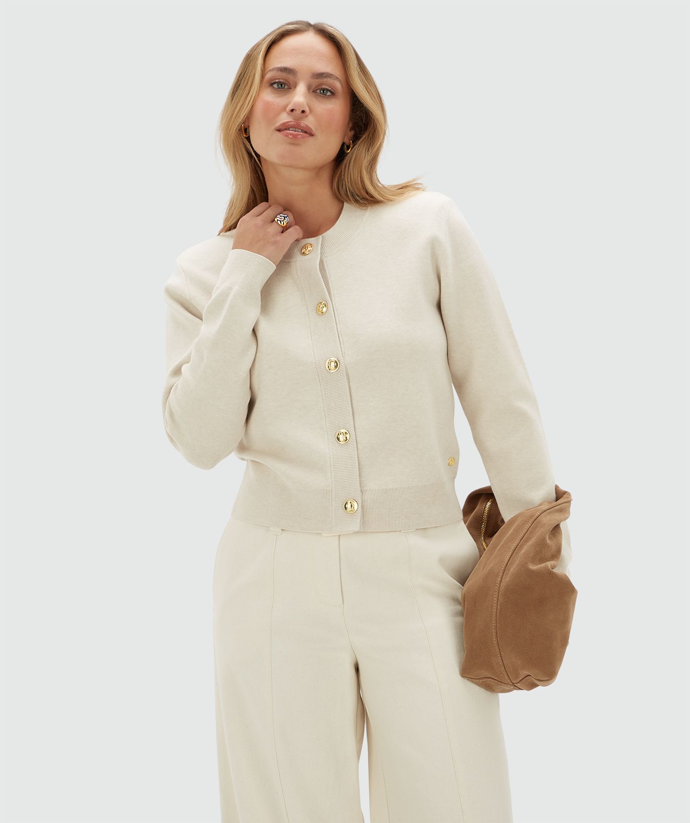 Model draagt een gebroken wit vest met gouden knopen en schoudervullingen op een beige broek.