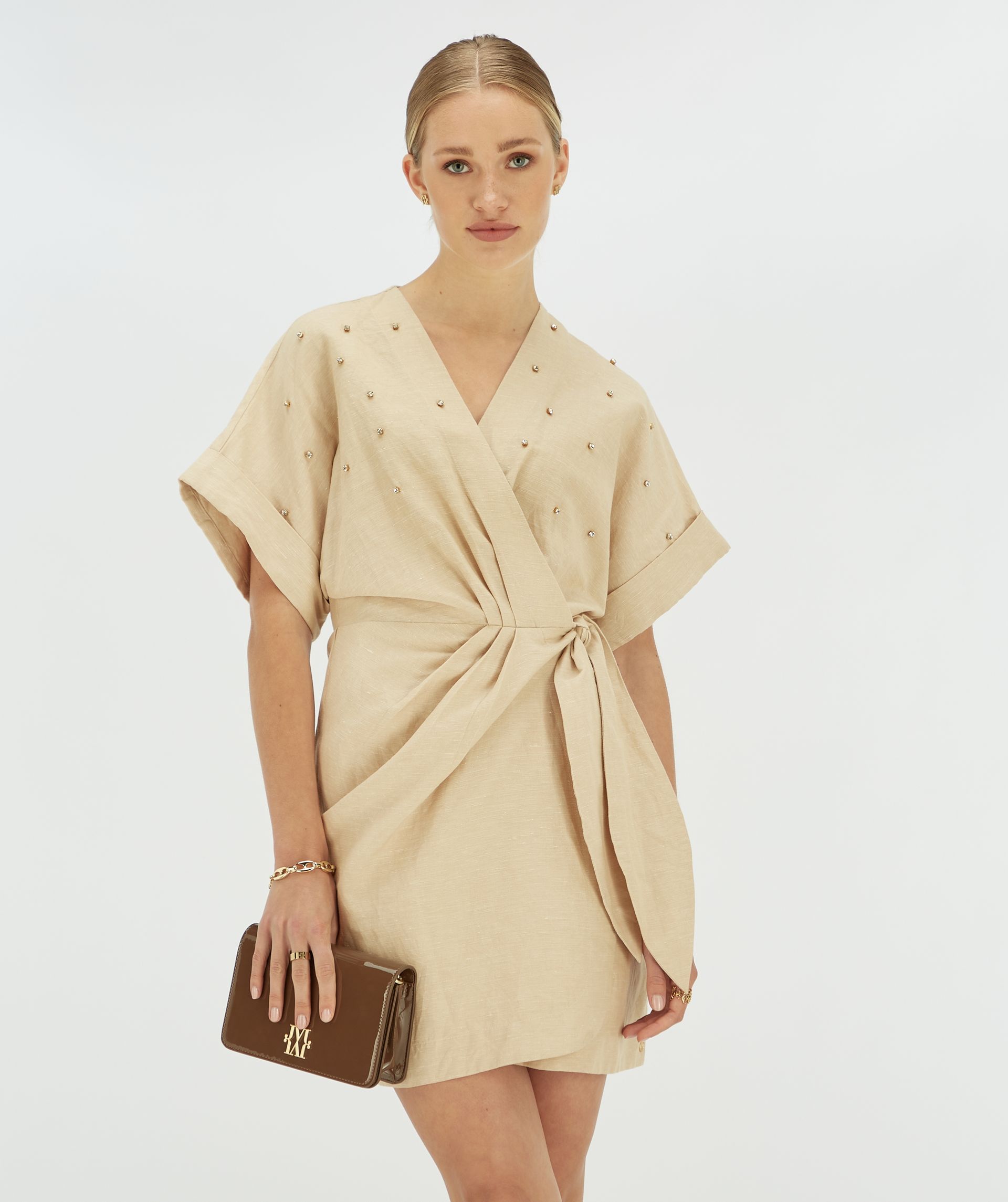 Model draagt beige overslagjurkje met sierstenen aan de voorkant.