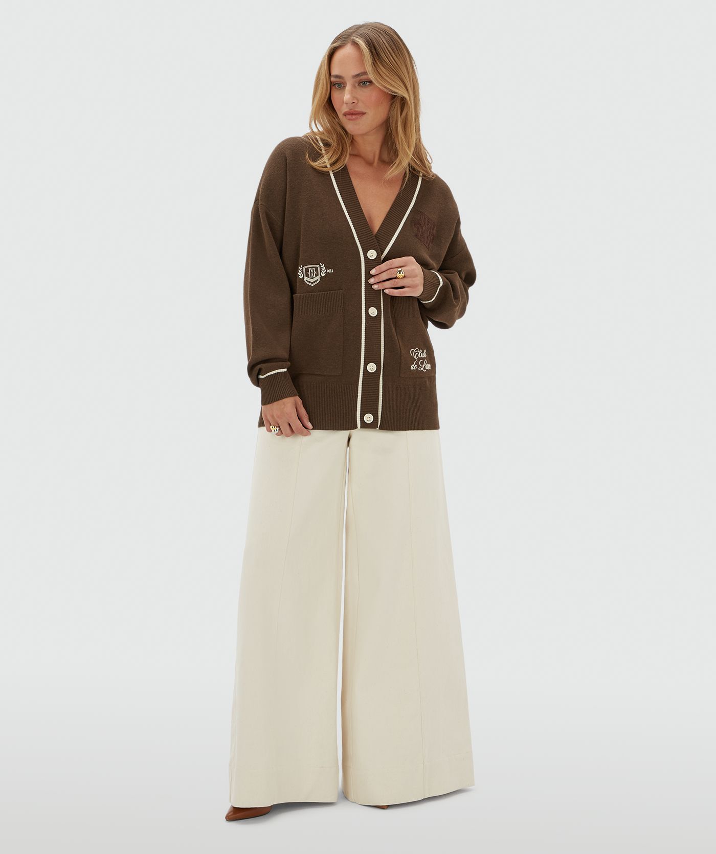 Model draagt een oversized donkerbruin vest met gebroken witte details. Het vest heeft ook twee steekzakken aan de voorkant. 