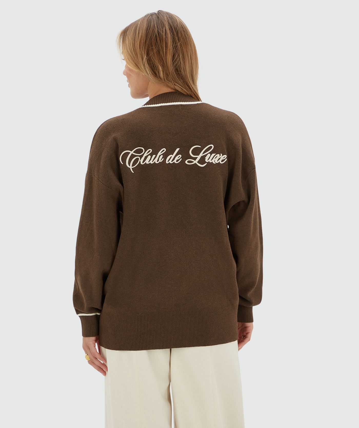 Achteraanzicht van een model in een oversized donkerbruin vest met beige letters op de achterkant.