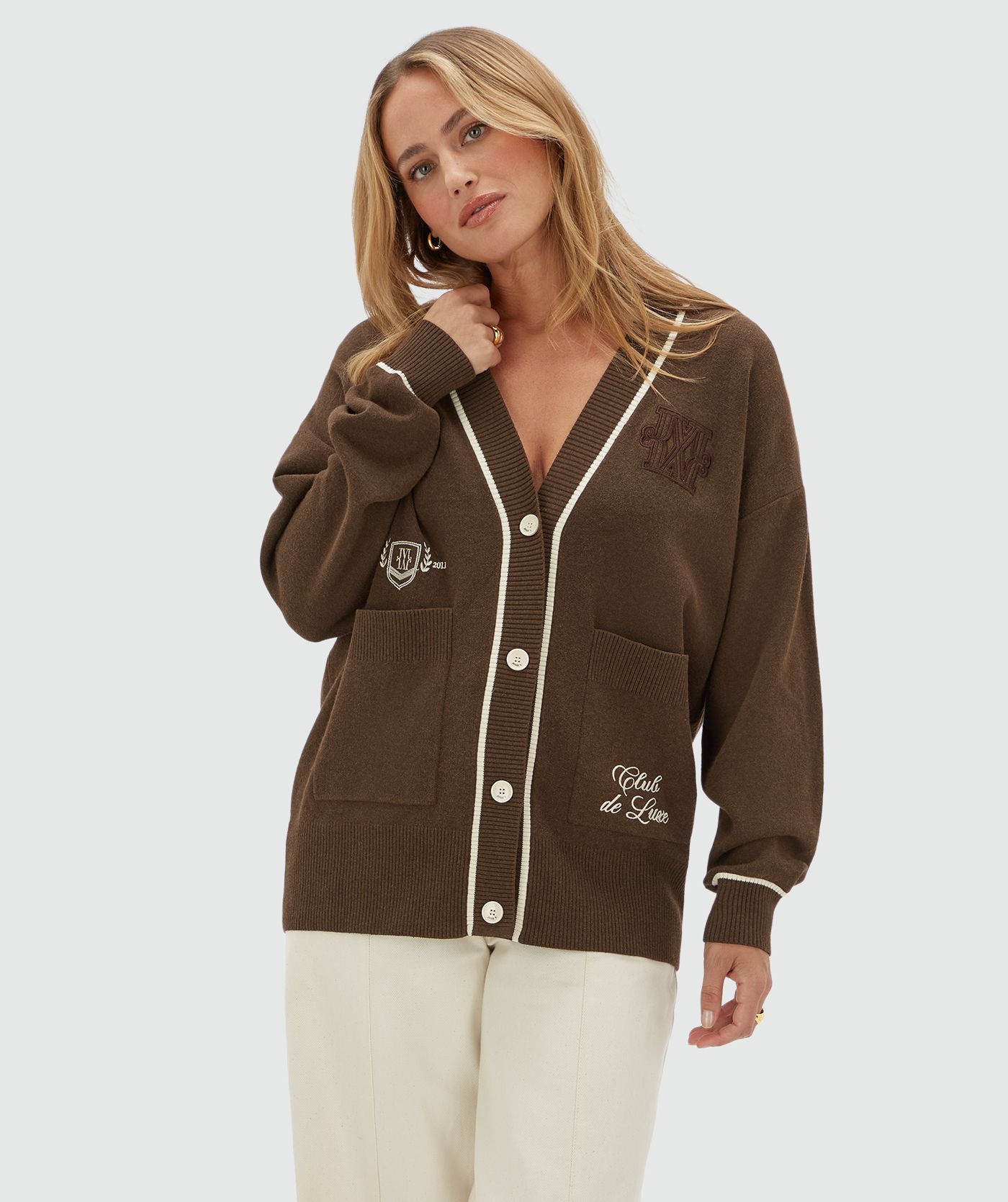 Model draagt een oversized donkerbruin vest met gebroken witte details. Het vest heeft ook twee steekzakken aan de voorkant. 