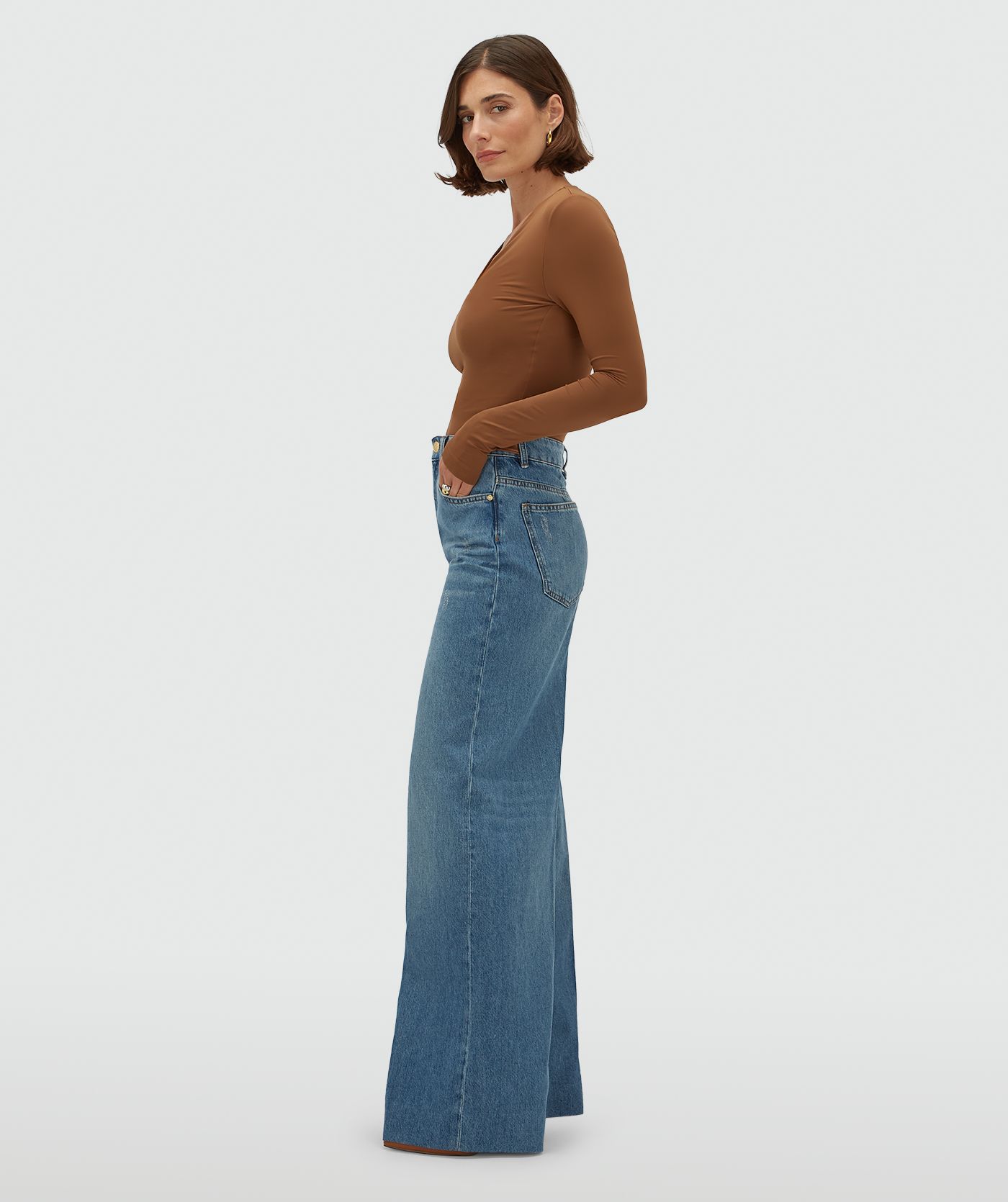 Model draagt een jeans met leren details aan de bovenkant, gecombineerd met een cognackleurige top.